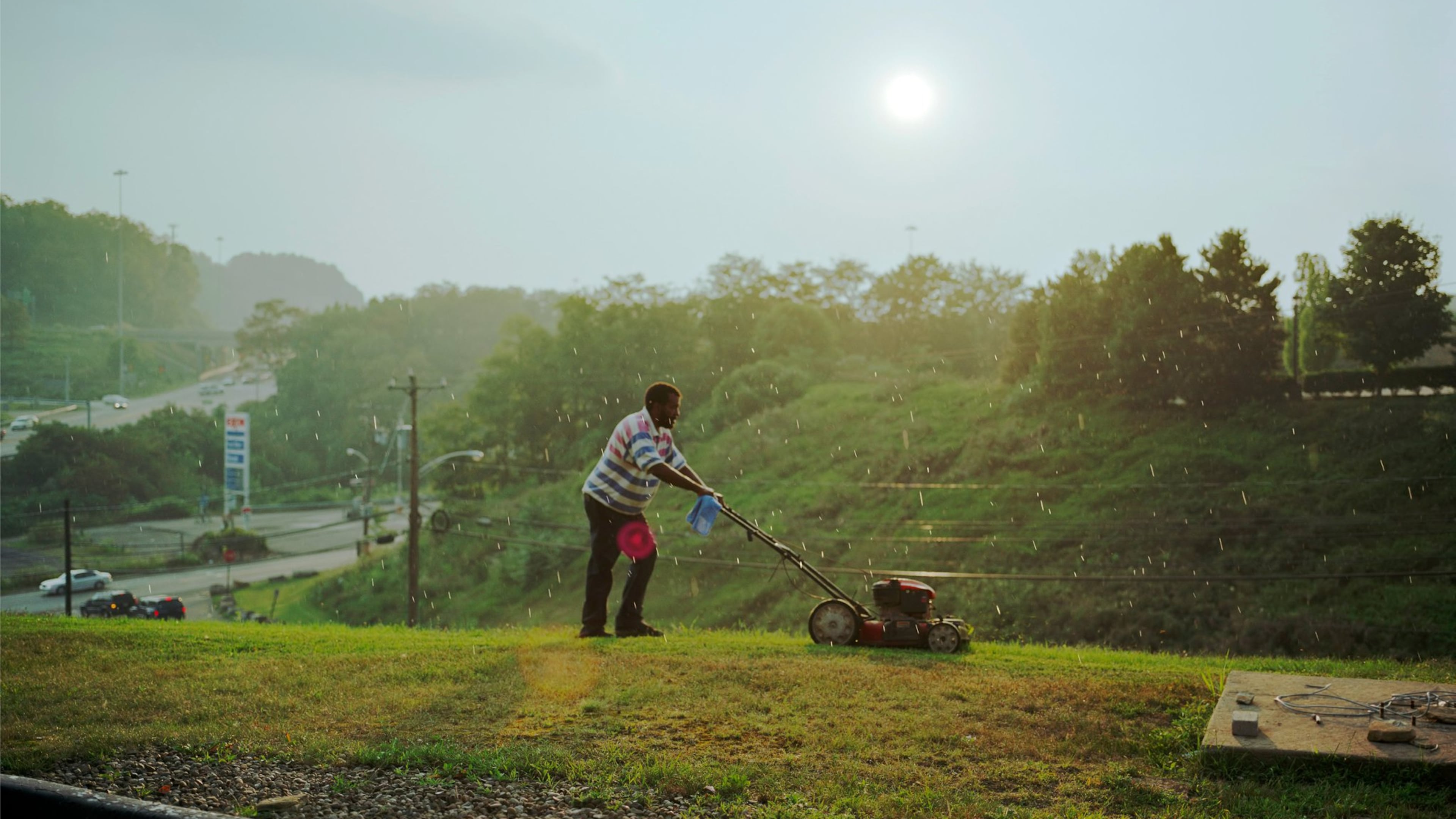 Paul Graham’s “Pittsburgh (detail)” captures the typically overlooked effort of a man mowing the grass on a steep hillside at a generic highway exit of cheap motels and gas stations. COPYRIGHT PAUL GRAHAM / CONTRIBUTED BY PACE/MACGILL GALLERY, NEW YORK
