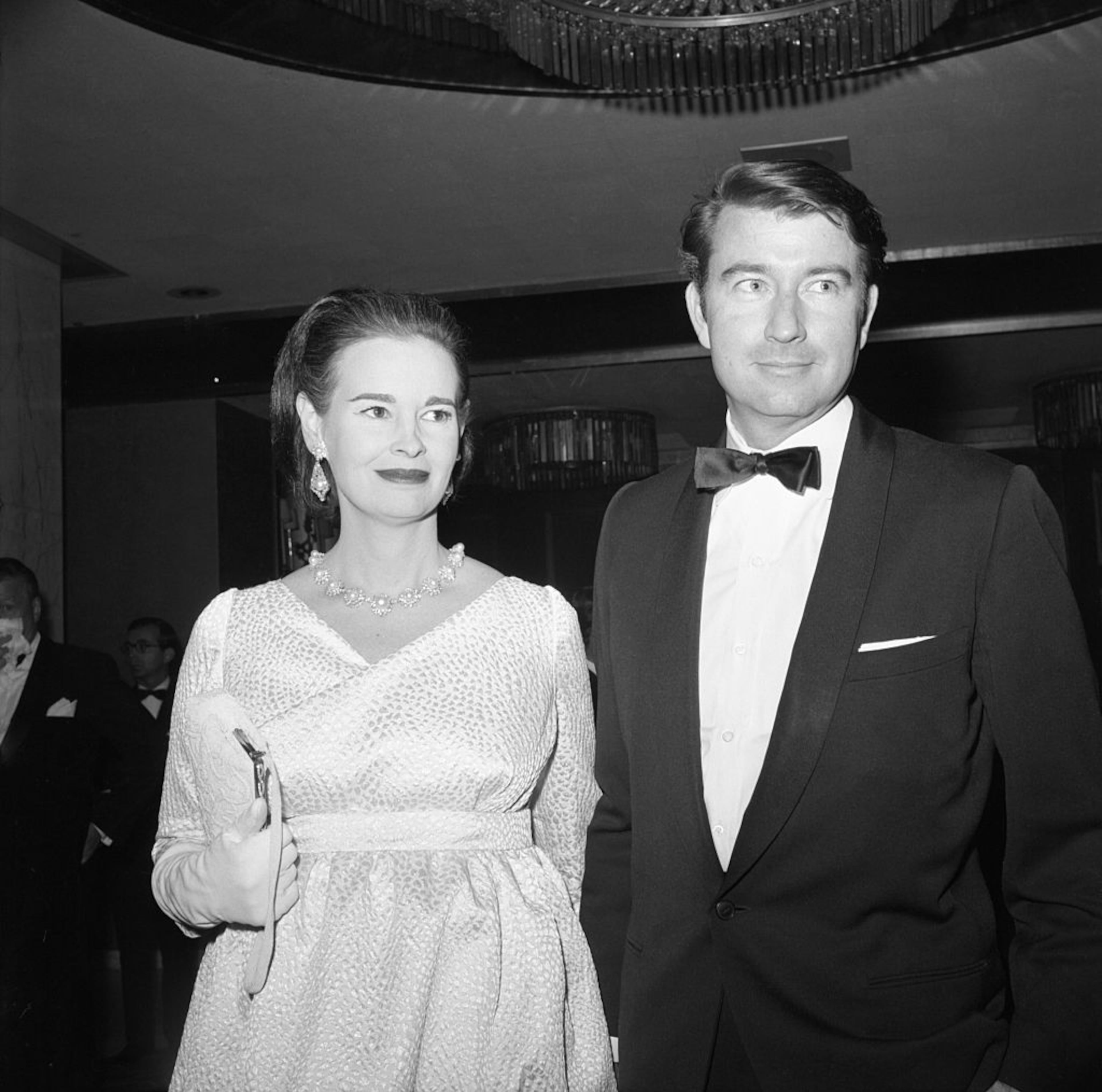 Mrs. Wyatt Cooper, better known as Gloria Vanderbilt, peeks over the shoulder of her husband and gives the cameraman a big smile as she arrives at the Criterion Theater, Oct 21, for the world premiere of the movie version of âMy Fair Lady.'