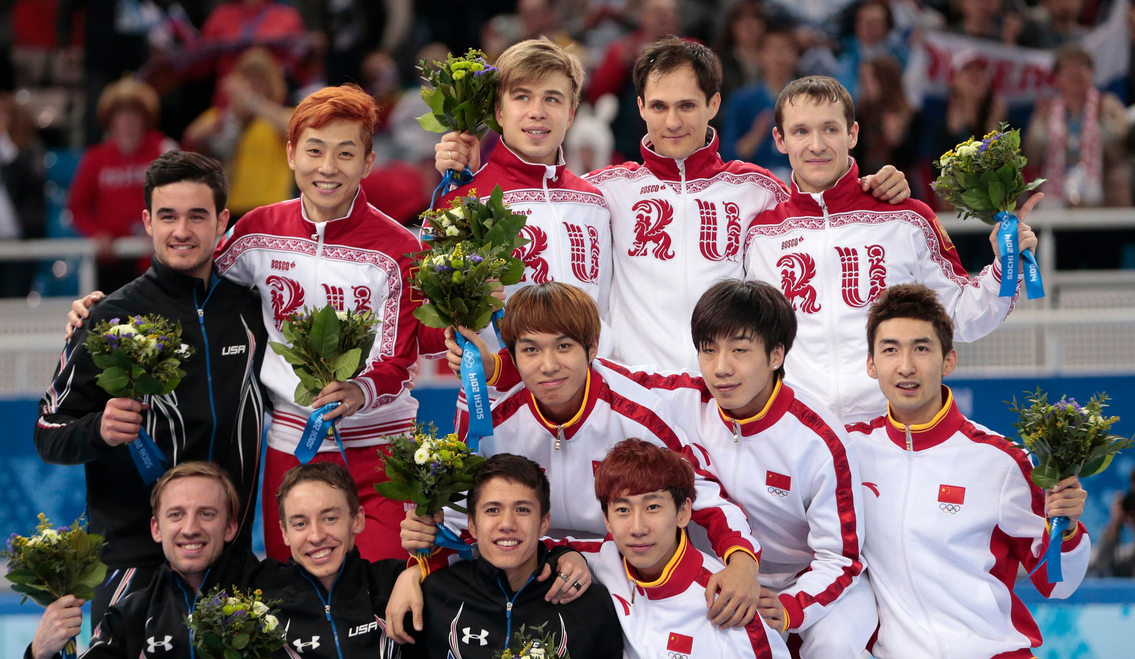 The Russian team, standing centre back, the U.S. team, at left in black, and the Chinese team, crouching at right, pose on the podium during the flower ceremony for the men's 5000m short track speedskating relay final at the Iceberg Skating Palace during the 2014 Winter Olympics, Friday, Feb. 21, 2014, in Sochi, Russia. Russia finished first, followed by the United States and China. (AP Photo/Ivan Sekretarev)