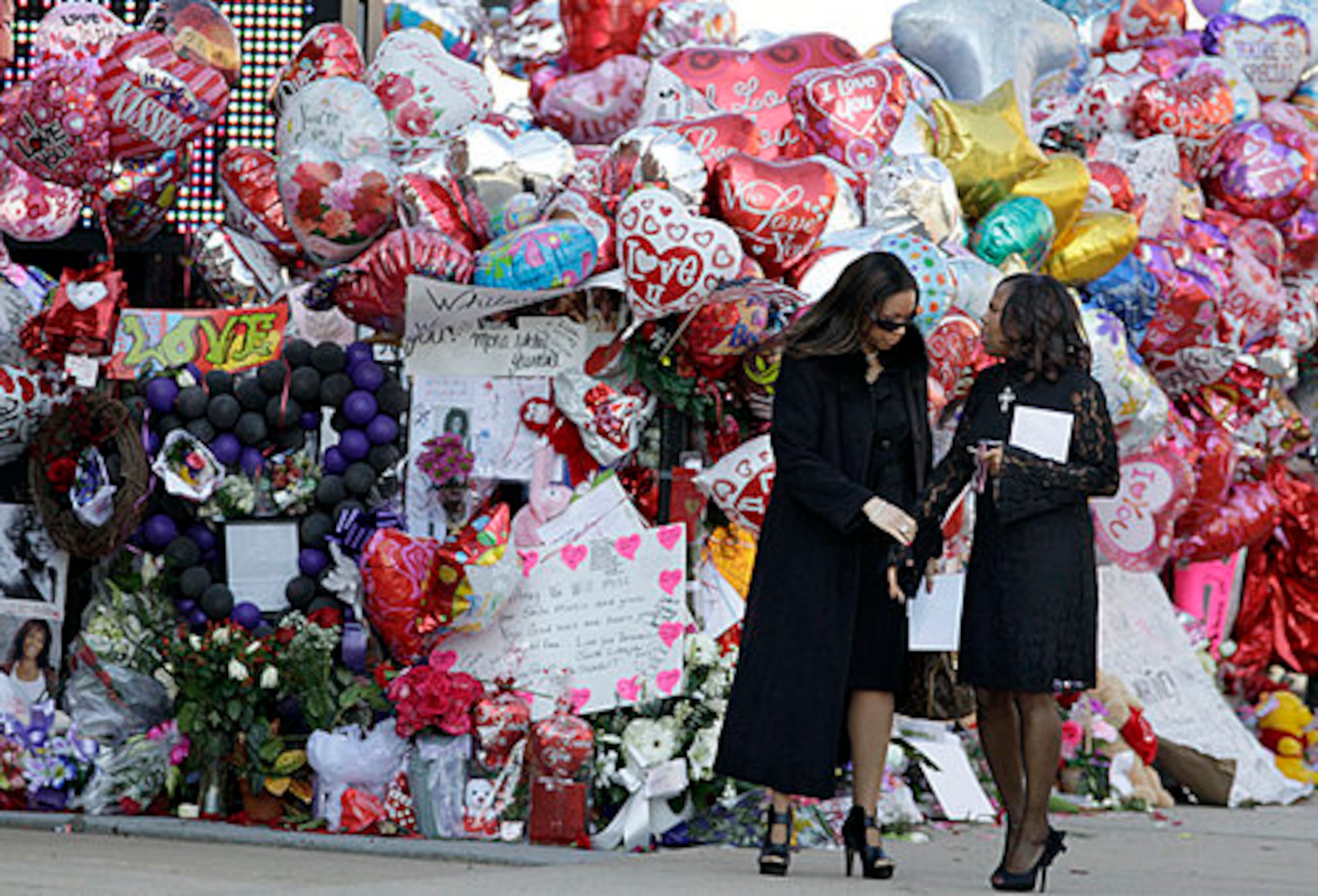 Two women pause near a memorial display before funeral services for singer Whitney Houston at the New Hope Baptist Church in Newark, N.J., Saturday, Feb. 18, 2012.