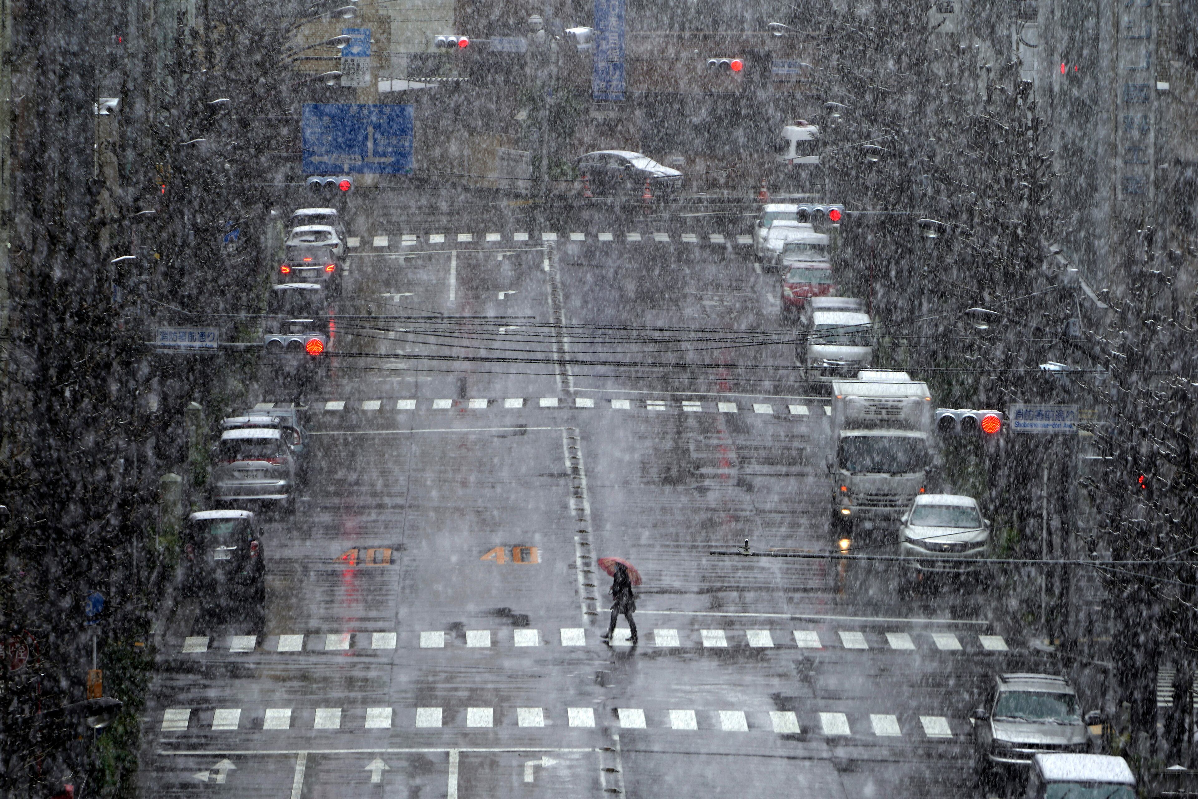 A woman walks in falling snow Saturday in Tokyo. Tokyo Gov. Yuriko Koike has repeatedly asked the city’s 13 million residents to stay home this weekend, saying the capital is on the brink of an explosion in virus infections.