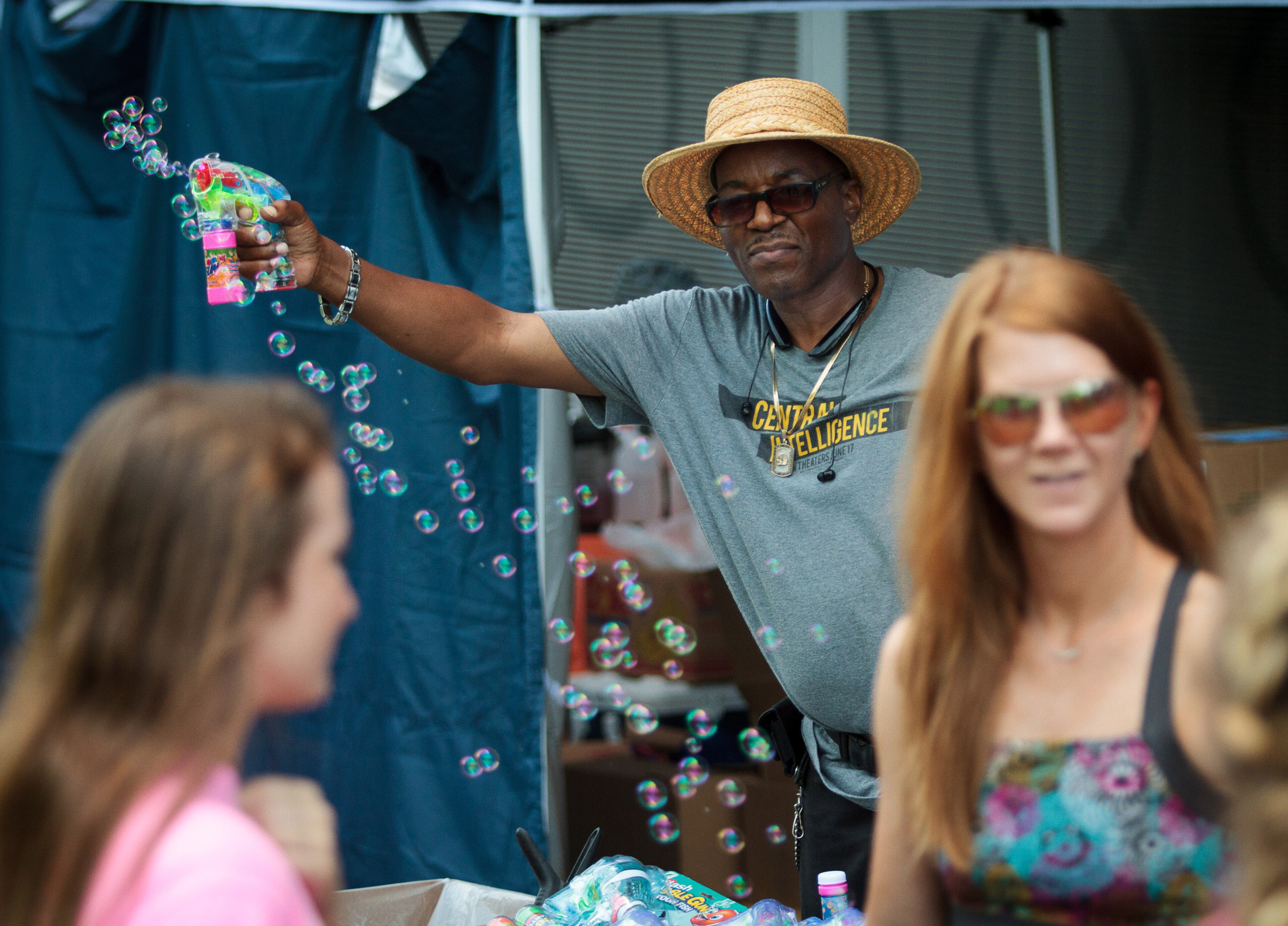 Vender Rau Alexander tries to get people to buy his bubble gun as they walk back up to the starting line of the 1,000-foot water slide at the Slide the City block party in Atlanta on Saturday, June 25, 2016. STEVE SCHAEFER / SPECIAL TO THE AJC