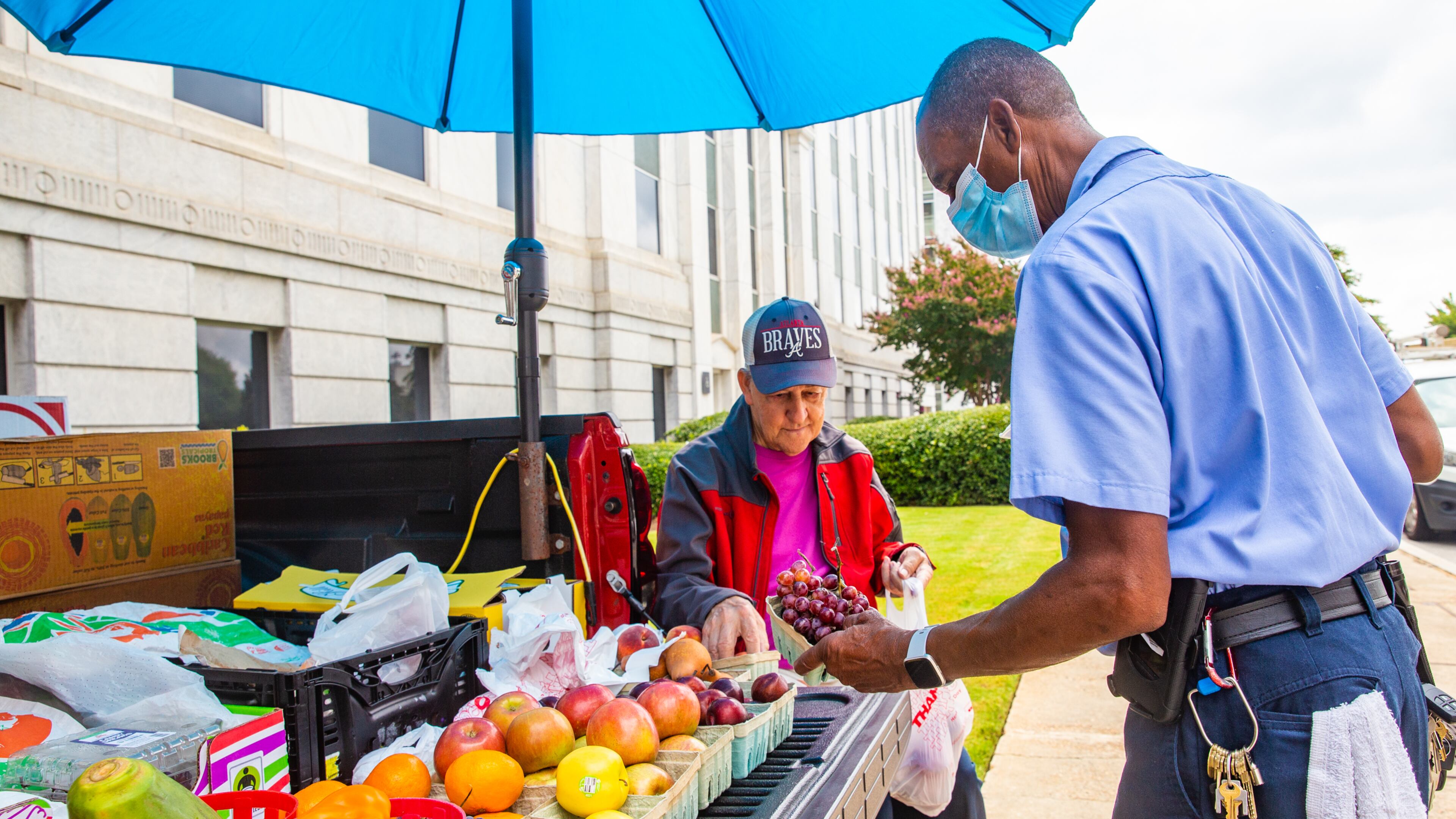 Gerald Reid, seated, who has been a mainstay for more than 50 years around the Atlanta state capitol campus, sells fresh fruits and vegetables out of the back of his truck to Eddie Ferrell, right, who works for the Georgia Building Authority, along Trinity Ave in Downtown Atlanta on Tuesday, Aug. 3, 2021. Reid, 79, comes downtown every week day from Fayetteville after a stop at his local farmers market to sells produce to those passing by, including Ferrell who is a regular customer and made note that Reid was missed on Monday, when he wasn't able to come. (Jenni Girtman for The Atlanta Journal Constitution)