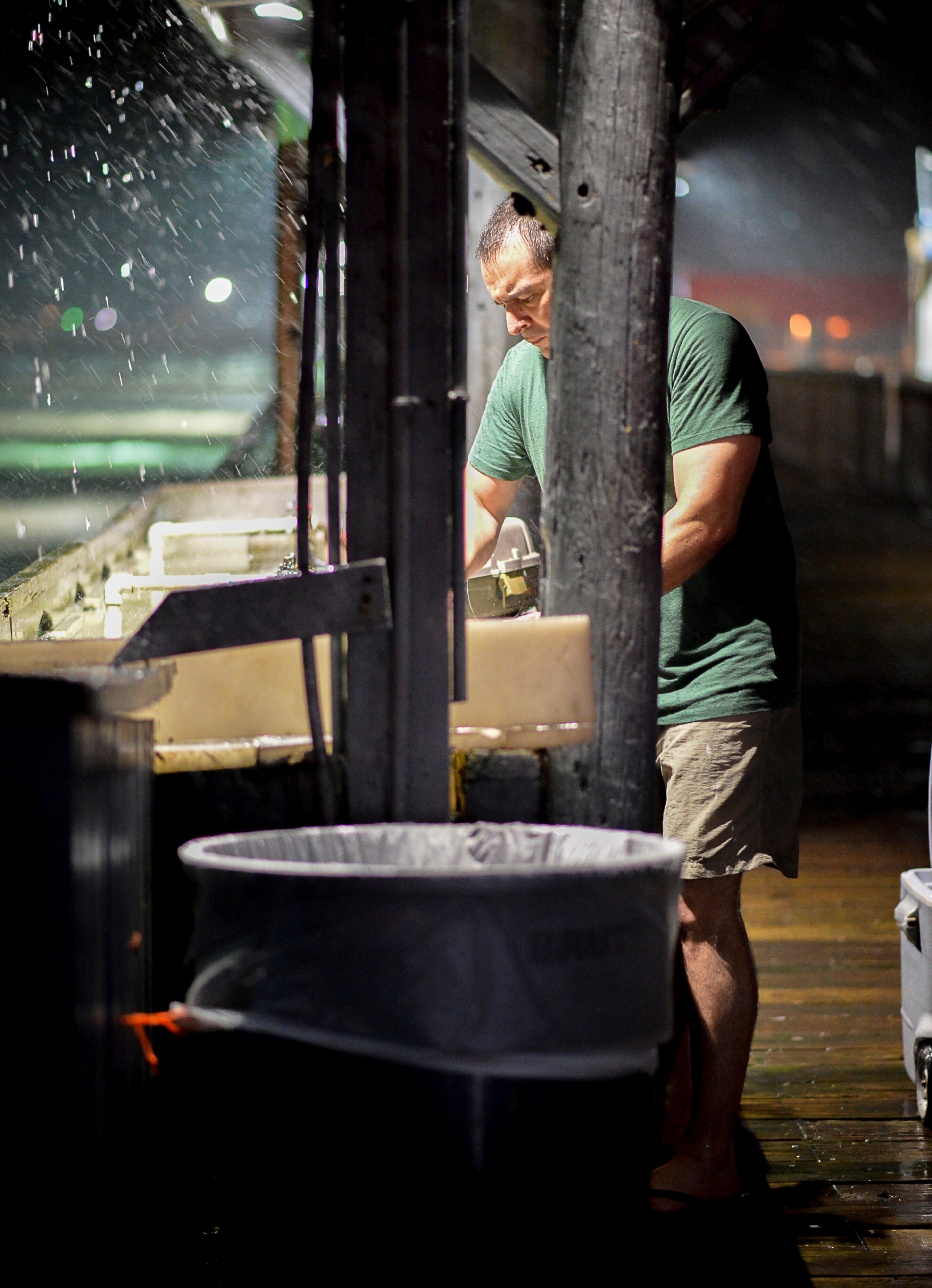 Steve Vega cleans his catch as wind-blown rain falls at a fishing pier on Thursday, Aug. 24, 2017, in Port Isabel, Texas. The deep South Texas town and surrounding communities are expected to receive several inches of rain and damaging winds as Hurricane Harvey passes along the coast toward the Texas Coastal Bend. (Jason Hoekema/The Brownsville Herald via AP)