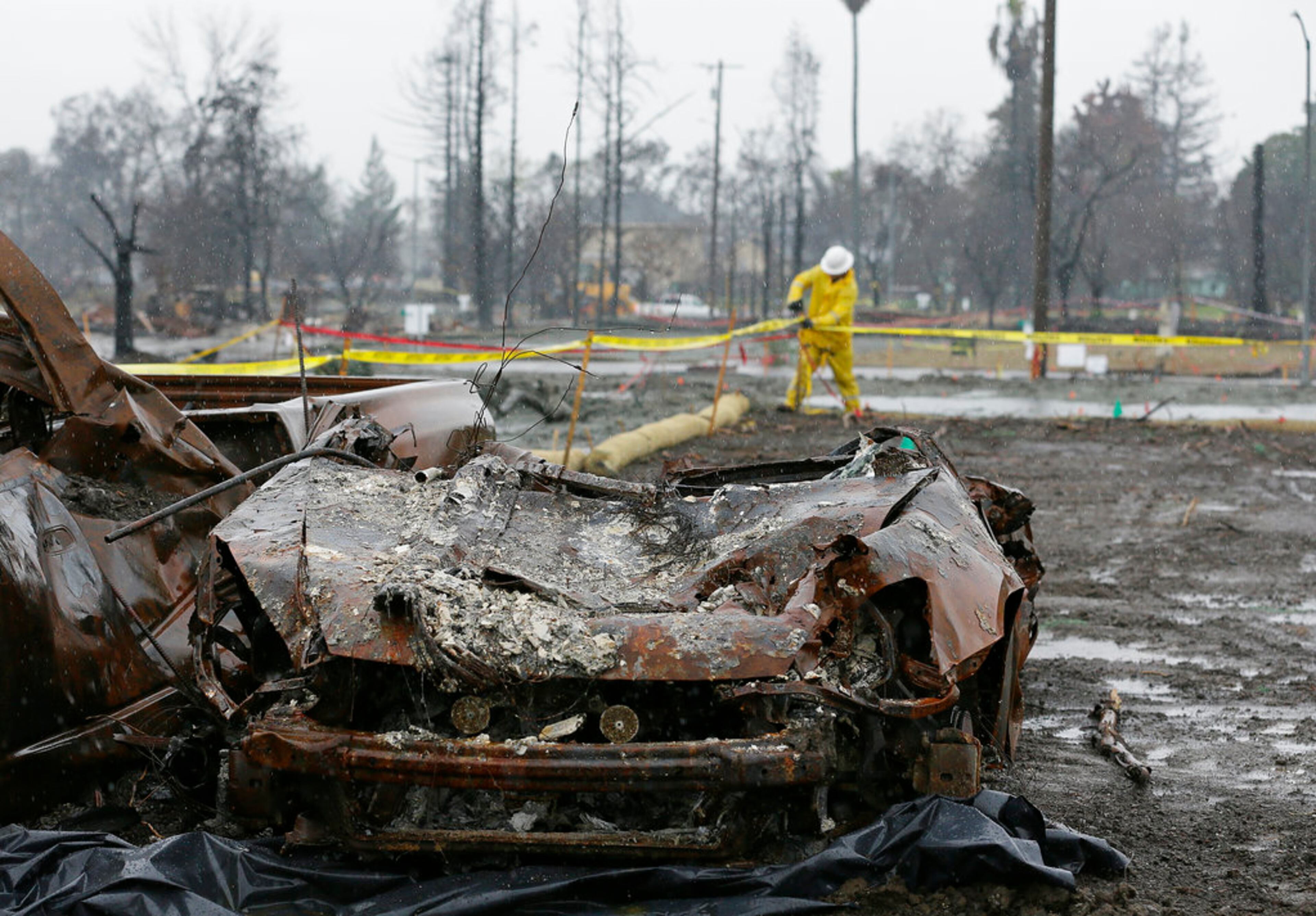 With a burned car in the foreground a worker finishes up erosion control efforts in the wildfire damaged Coffey Park neighborhood, Monday, Jan. 8, 2018, in Santa Rosa, Calif. Storms brought rain to California on Monday and increased the risk of mudslides in fire-ravaged communities in devastated northern wine country and authorities to order evacuations farther south for towns below hillsides burned by the state's largest-ever wildfire. (AP Photo/Eric Risberg)
