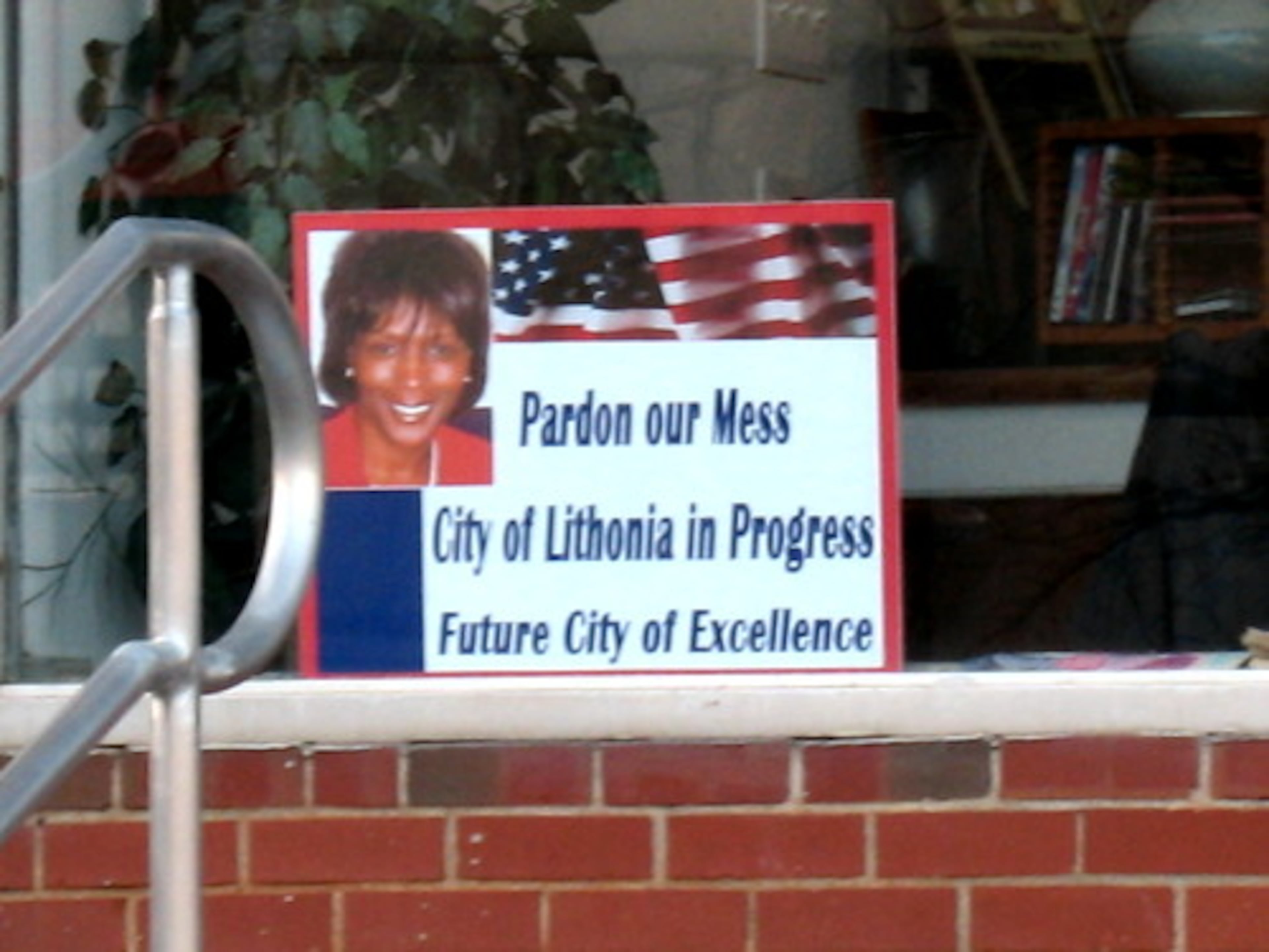 Lithonia's political drama came to light recently when Mayor Joyce McKibben fired Police Chief Willie Rosser. Then, the city council hired Rosser back.This poster, featuring McKibben, is posted in the window of a coffee shop in the town's city square. "Pardon our mess," it says.