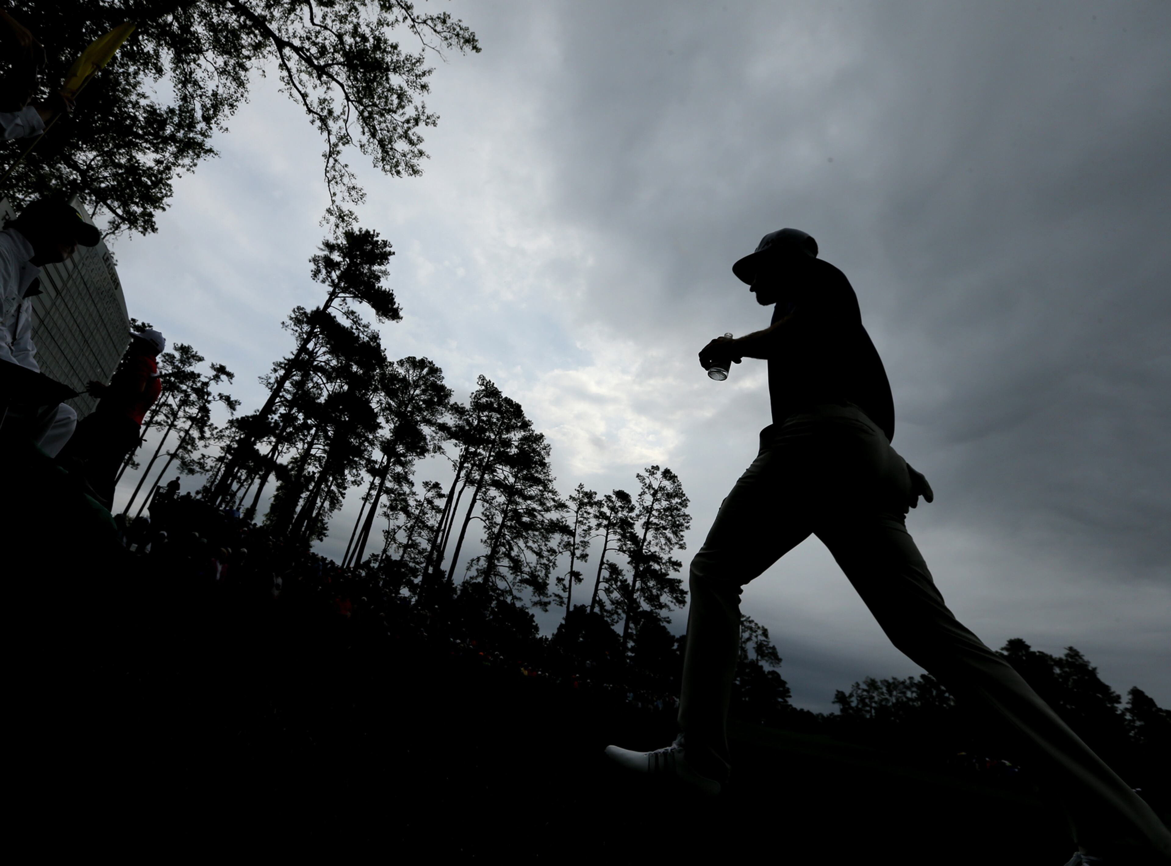 Dustin Johnson walks to the 14th tee box under a darkening sky before play is suspended.