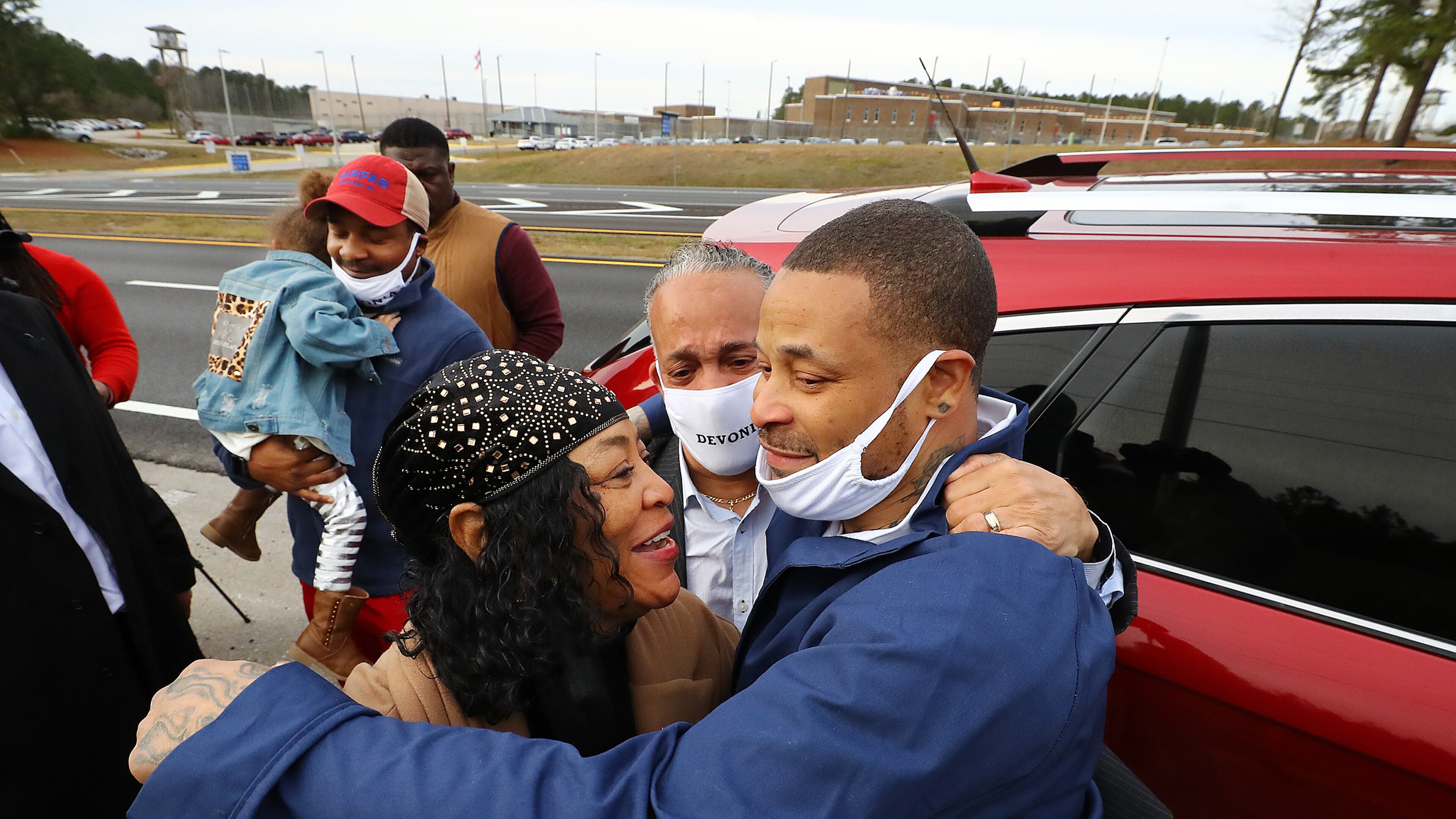 Devonia Inman is embraced by his mother, Dinah Ray, and stepfather, David Ray, after being released from custody Dec. 20, 2021, from the Augusta State Medical Prison (background) after serving 23 years for a wrongful conviction. His charges were dismissed in a murder case. Legislation has been proposed to give Inman more than $1.6 million as compensation for the time he was incarcerated. Curtis Compton / Curtis.Compton@ajc.com