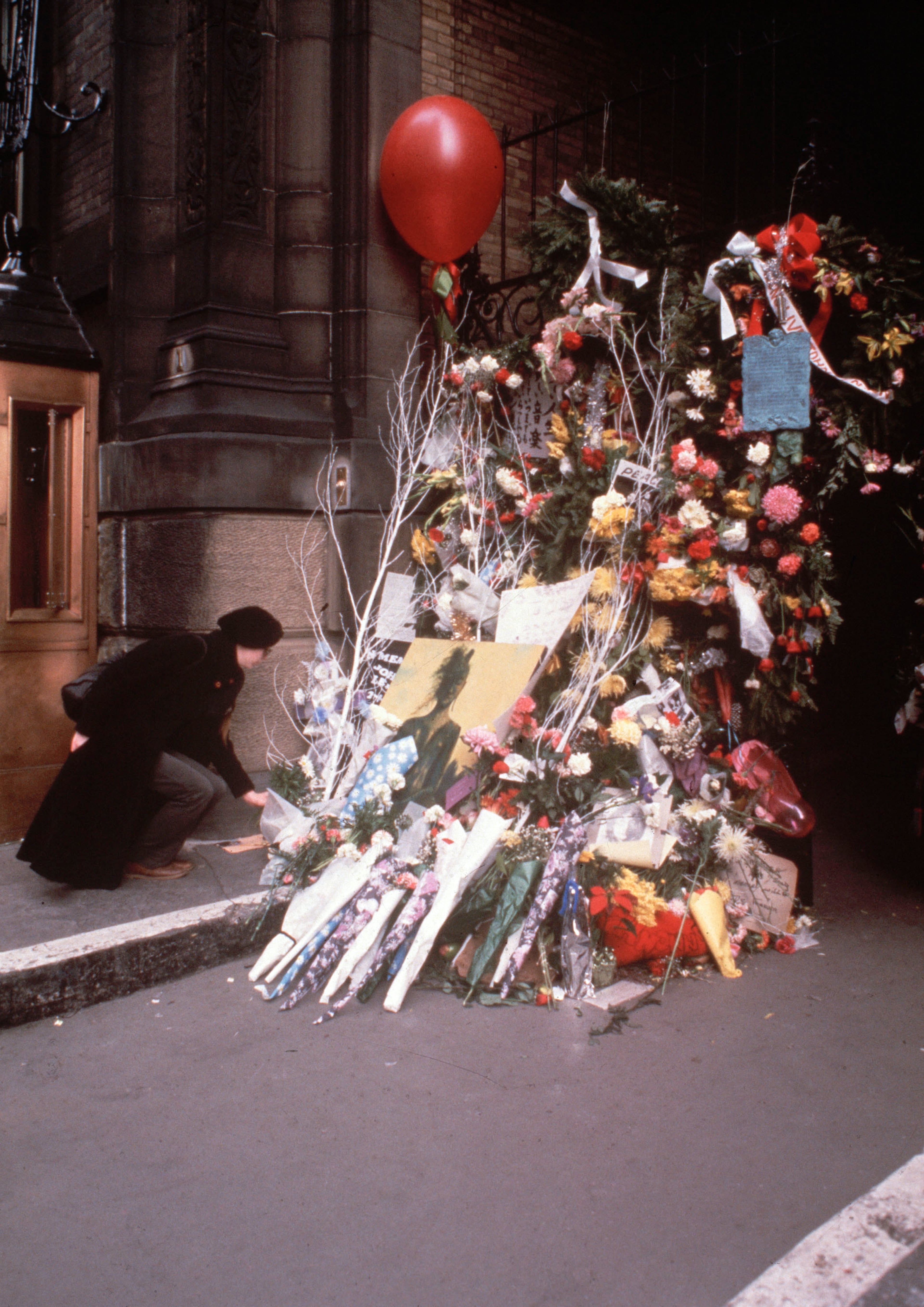 In this 1980 file photo, a woman leaves flowers at a make shift memorial outside the Dakota apartment house where John Lennon was shot and killed on Monday, Dec. 8, 1980 in New York. The death of Lennon, shot 35 years ago, still reverberates as a defining moment for a generation and for the music world. (AP File Photo)