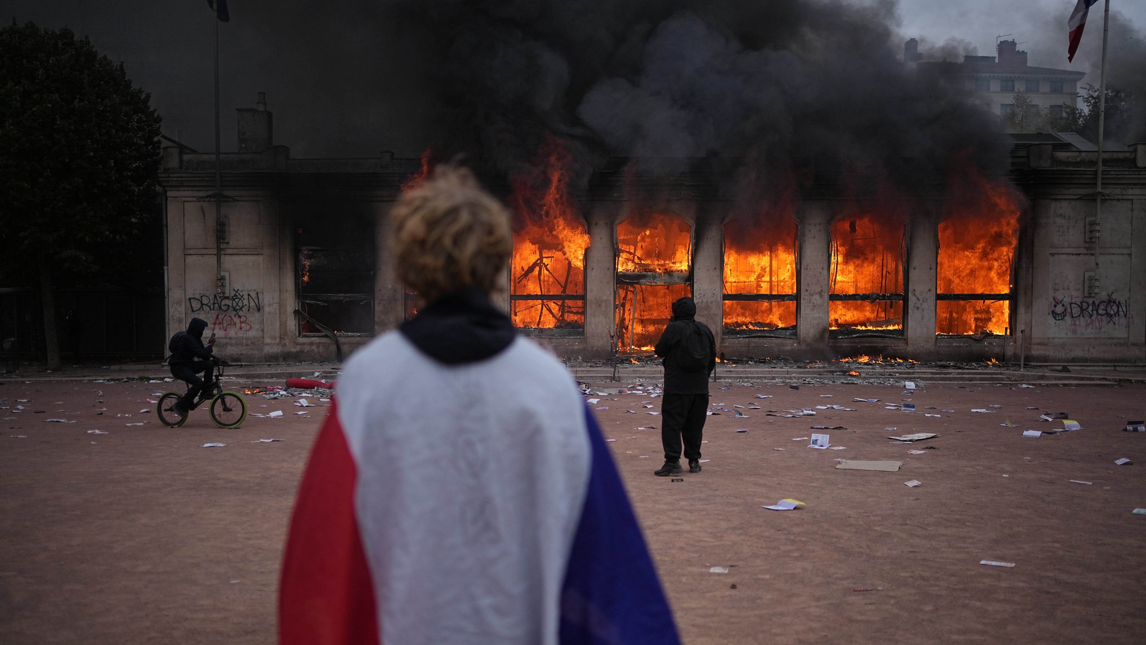 A protester wraps a French flag around them in front of the burning tourism office during a demonstration against rising living costs and in solidarity with students’ grievances in Lyon, France, Saturday, Oct. 17, 2026. (AP Photo/Laurent Cipriani)