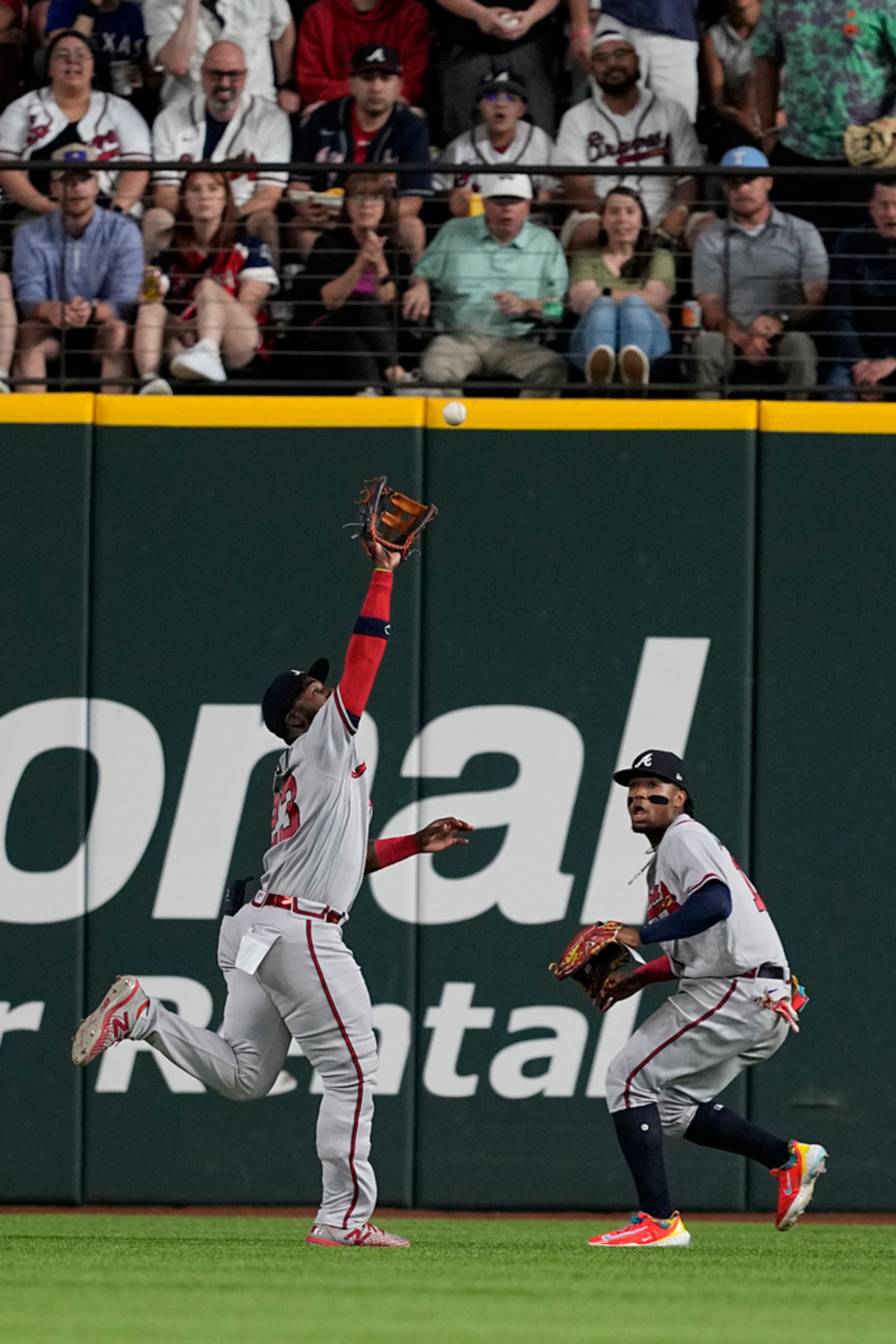 Fans and Atlanta Braves right fielder Ronald Acuna Jr., right, look on as center fielder Michael Harris II positions beneath a fly out hit by Texas Rangers' Jonah Heim in the fourth inning of a baseball game, Tuesday, May 16, 2023, in Arlington, Texas. (AP Photo/Tony Gutierrez)