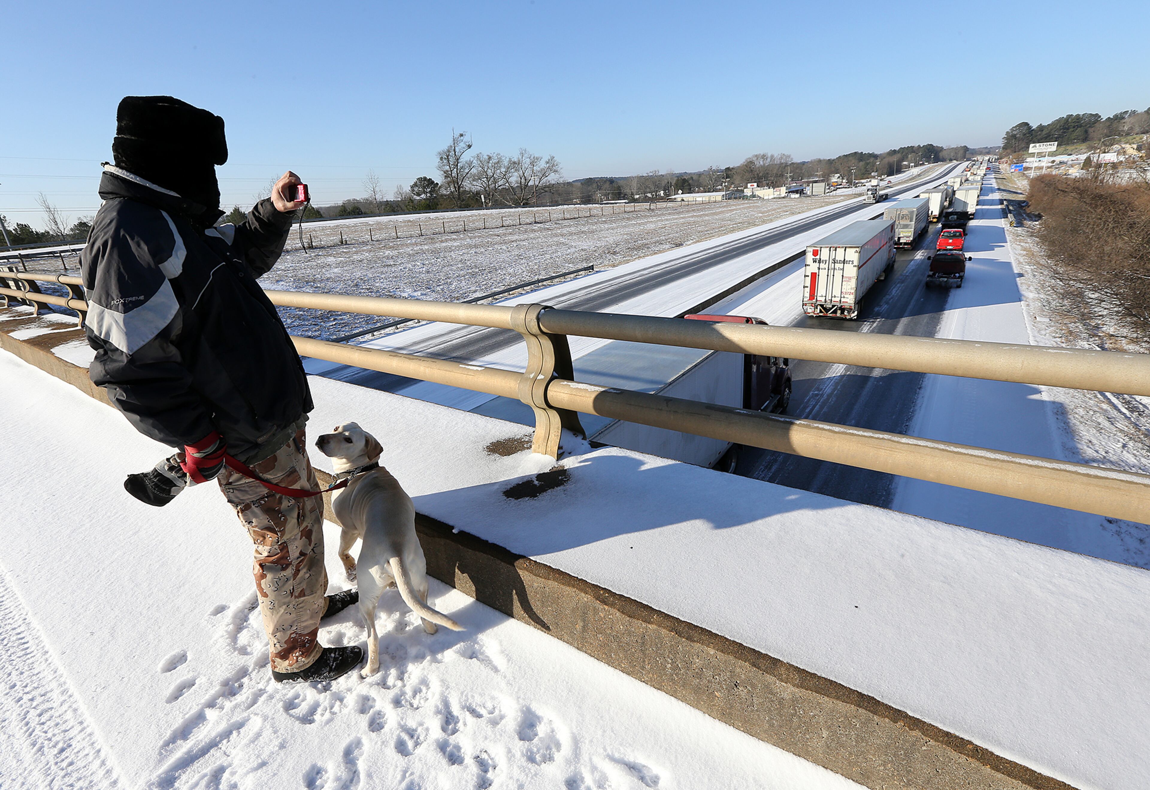 January 17, 2018 Covington: Paul Vaca stops to snap photos of the traffic jam while walking his dog Casper across a ice covered overpass at I-20 West near the Almon Road exit after multiple tractor trailer trucks jackknifed in the winter conditions closing the west bound lanes on Wednesday, January 17, 2018, in Covington. Curtis Compton/ccompton@ajc.com