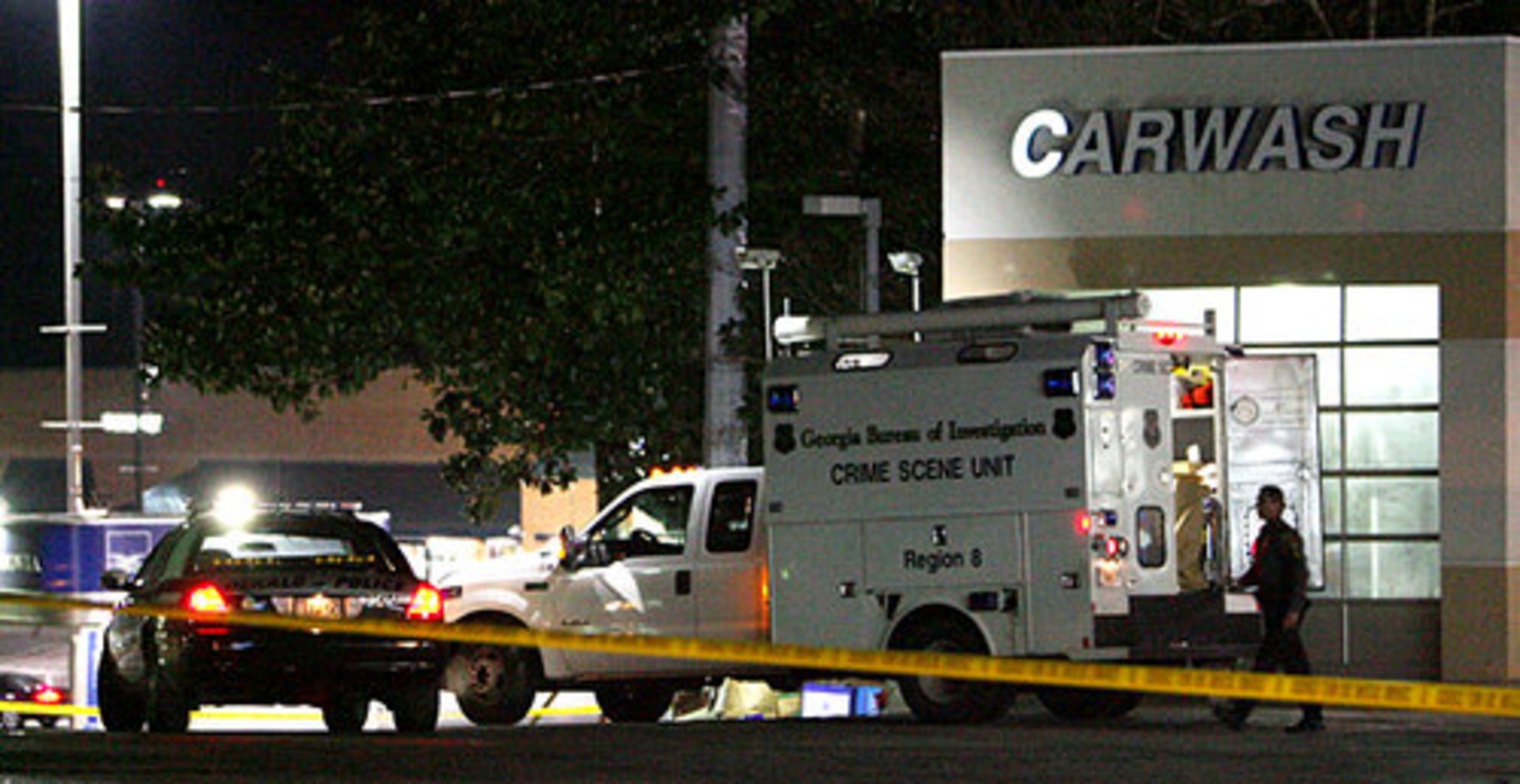 A DeKalb Police cruiser and a GBI Crime Scene truck are parked in front of a dumpster as investigators go through the garbage at a Chevron station.