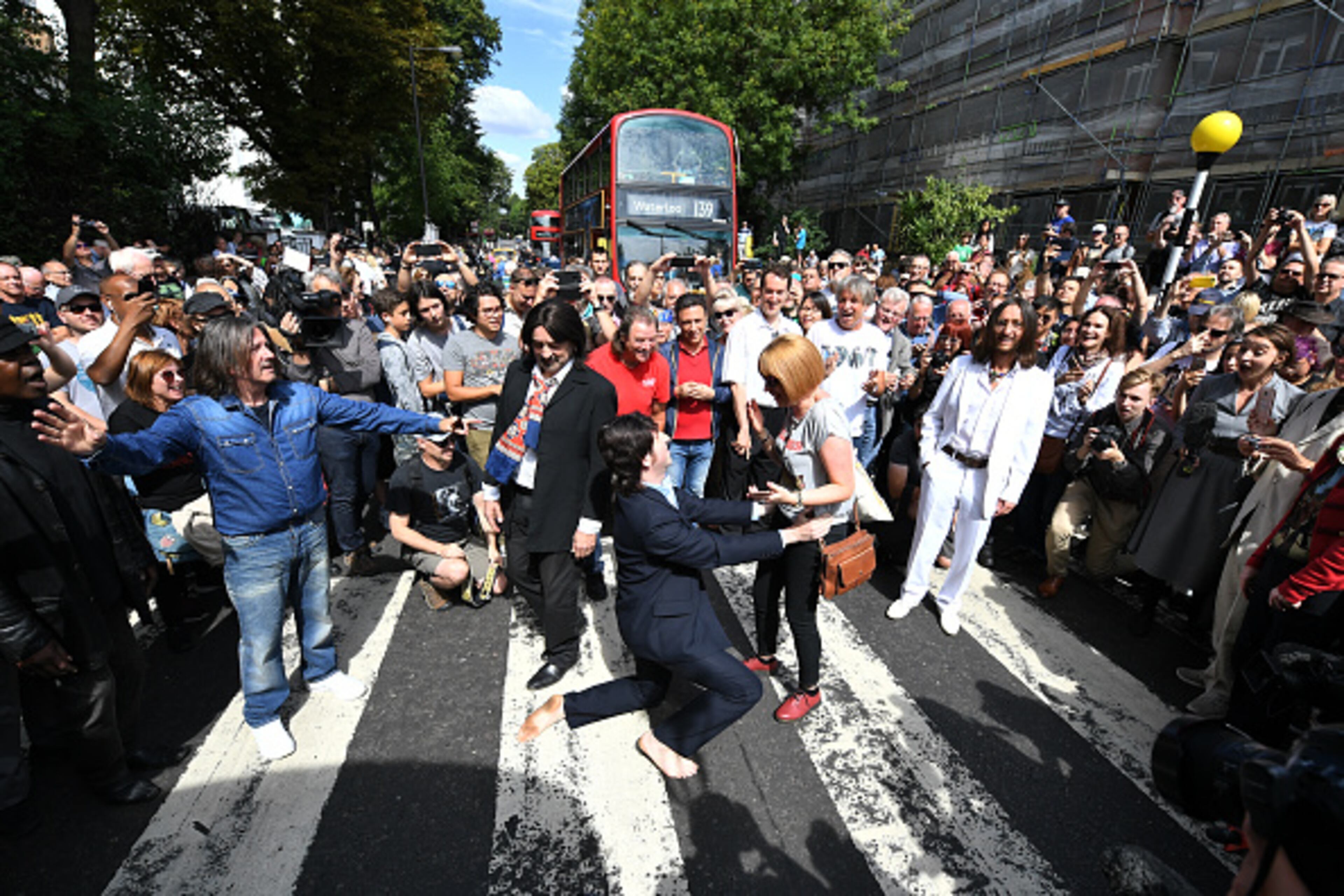 LONDON, ENGLAND - AUGUST 08: A Paul McCartney impersonator proposes to his girlfriend as a group of Beatles look-alikes recreate the iconic 'Abbey Road' photograph made 50 years ago today, on August 8, 2019 in London, England. 50 years ago today, John Lennon, Paul McCartney, George Harrison and Ringo Starr held up traffic on the zebra crossing outside their recording studio in north London to get the cover shot for the album, Abbey Road. (Photo by Leon Neal/Getty Images)