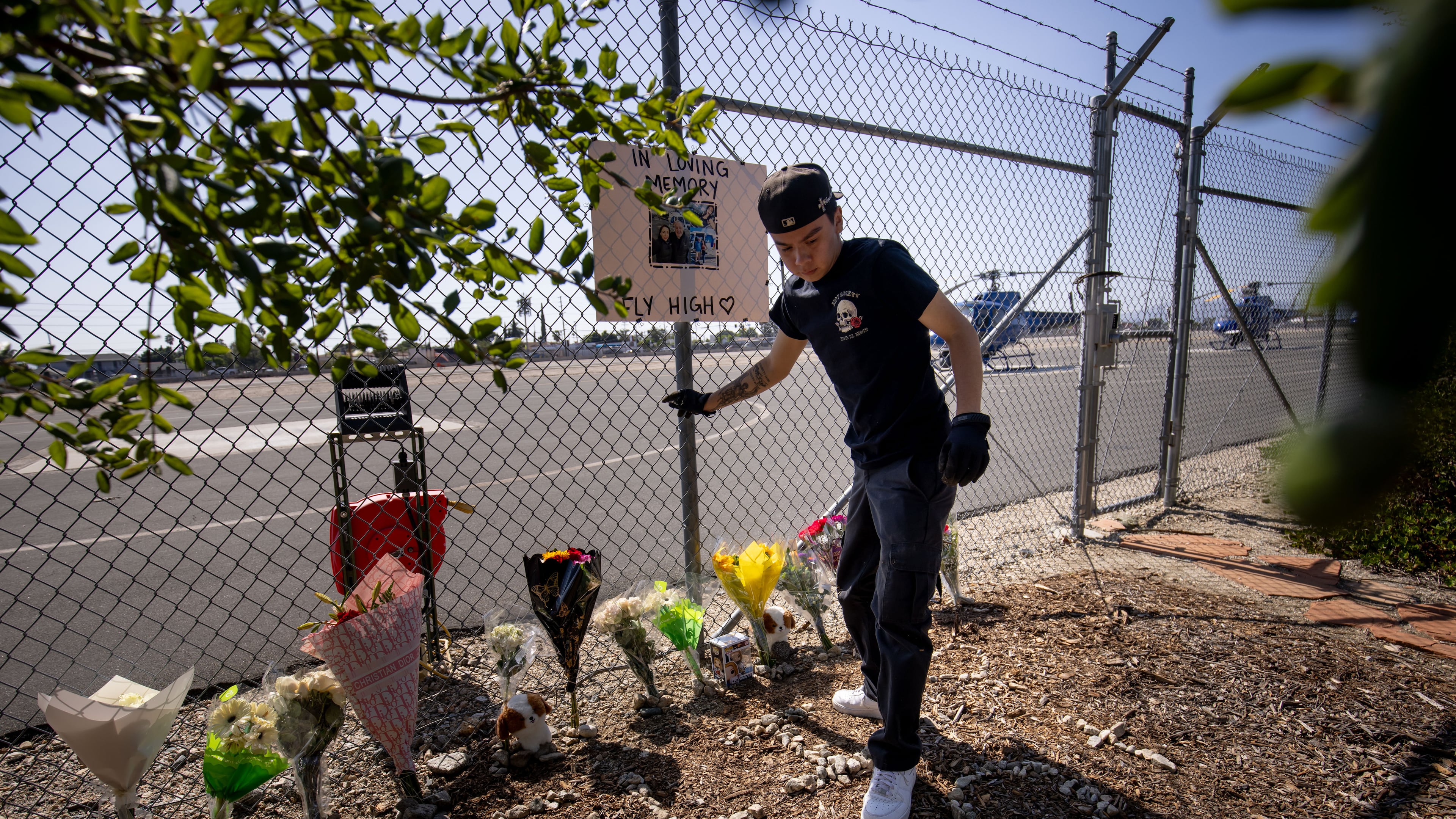 A person adjusts flowers at a memorial for Eliana Moreno and George Marciniw who died in a helicopter crash at the site where their helicopter used to park at Whiteman Airport in Los Angeles, Wednesday, Sept. 16, 2026. (AP Photo/Ethan Swope)