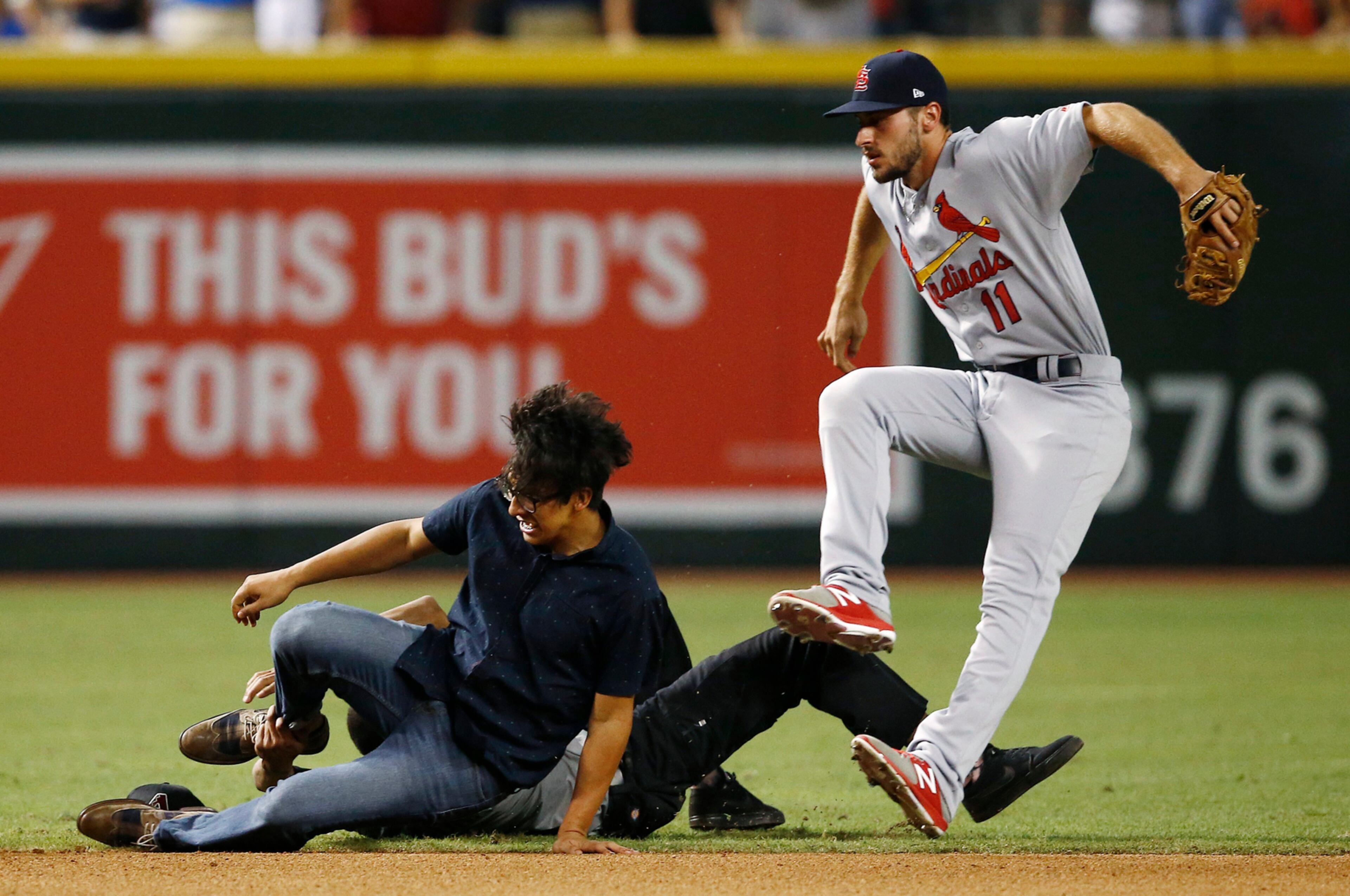 A spectator, left, gets tackled by a security guard as they both collide with St. Louis Cardinals' Paul DeJong (11) after the sixth inning of the Cardinals' baseball game against the Arizona Diamondbacks on Wednesday, June 28, 2017, in Phoenix. (AP Photo/Ross D. Franklin)