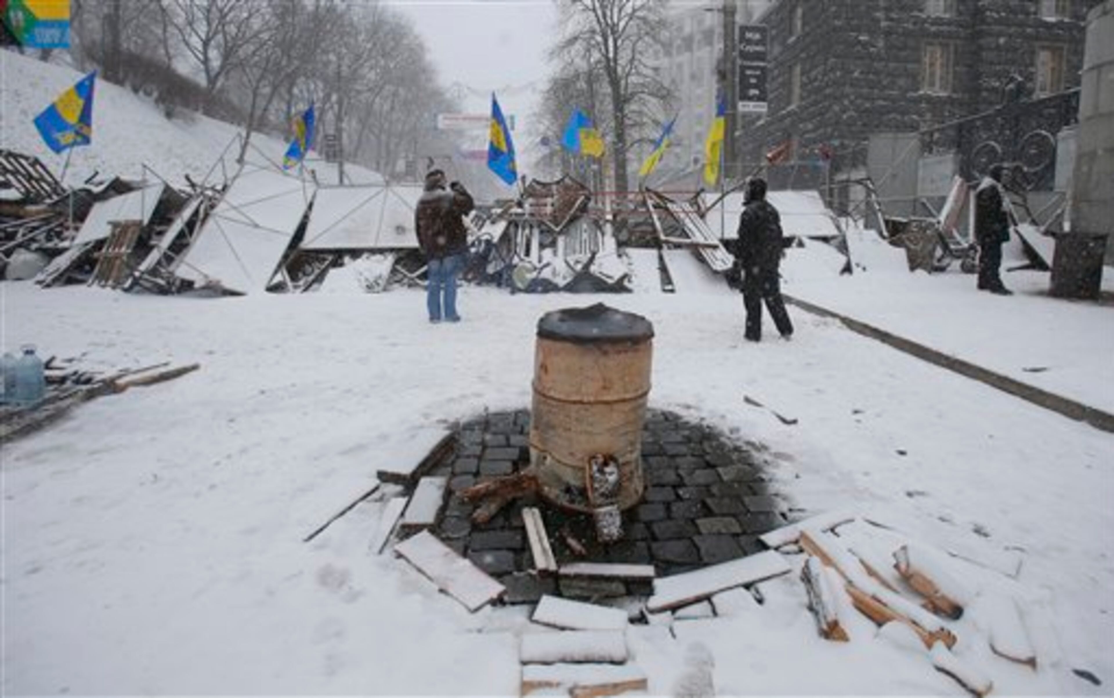 Pro-European Union activists stand behind snow covered barricades at Ukrainian presidential administration building in Kiev, Ukraine, Monday, Dec. 9, 2013. A bonfire is seen on foreground. The policemen, wearing helmets and holding shields, formed a chain across Kiev�s main street outside the city building. Organizers called on protesters to vacate the city hall and the other building which the opposition had used as its headquarters. (AP Photo/Sergei Grits)