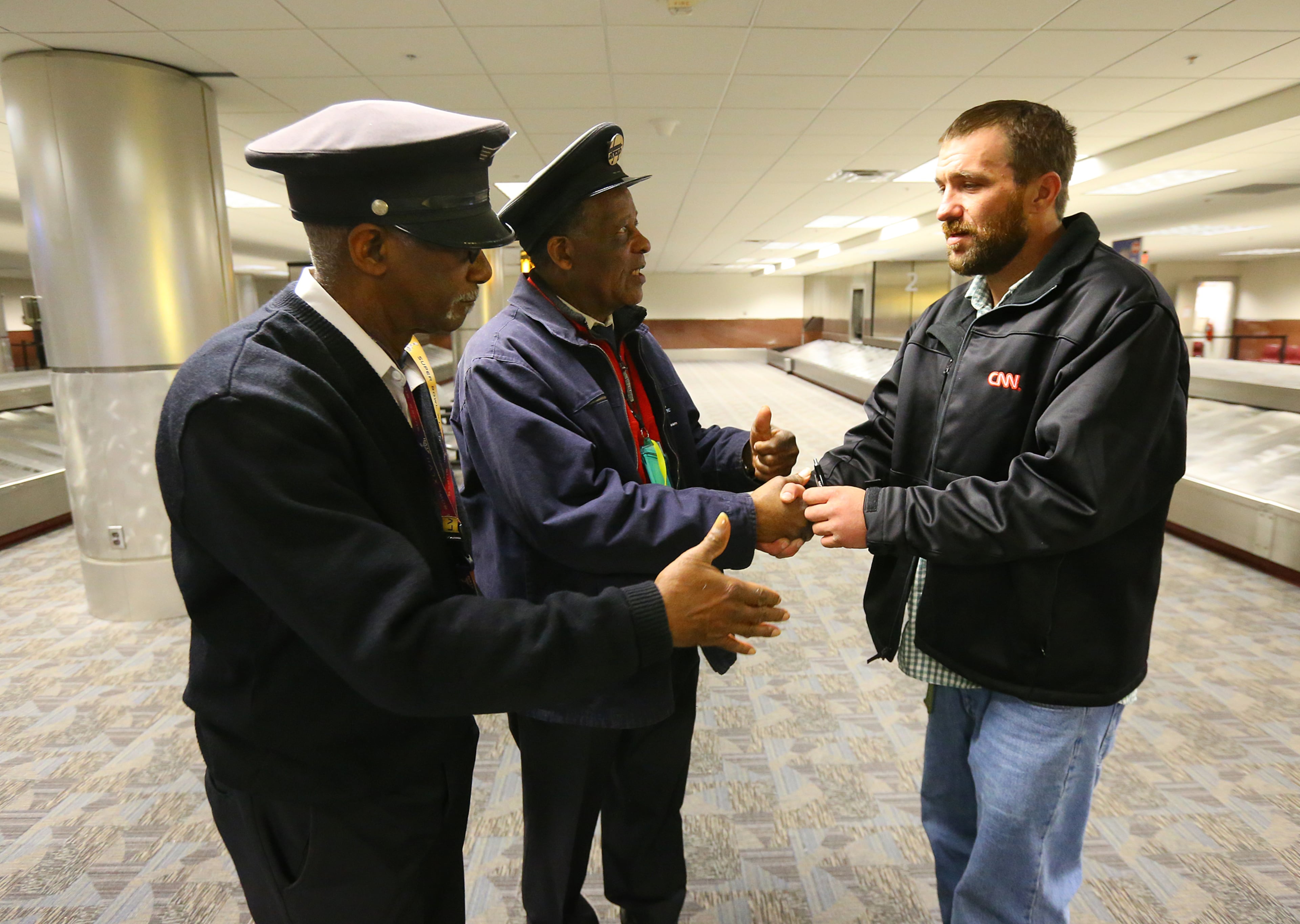 Primeflight Aviation Service employees Carl Worthy (left) and Lloyd Mitchell met "Homeless Hero" Joel Hartman at baggage claim as he is reunited with his family at Hartsfield Jackson Airport for Thanksgiving on Thursday, Nov. 28, 2013, in Atlanta.