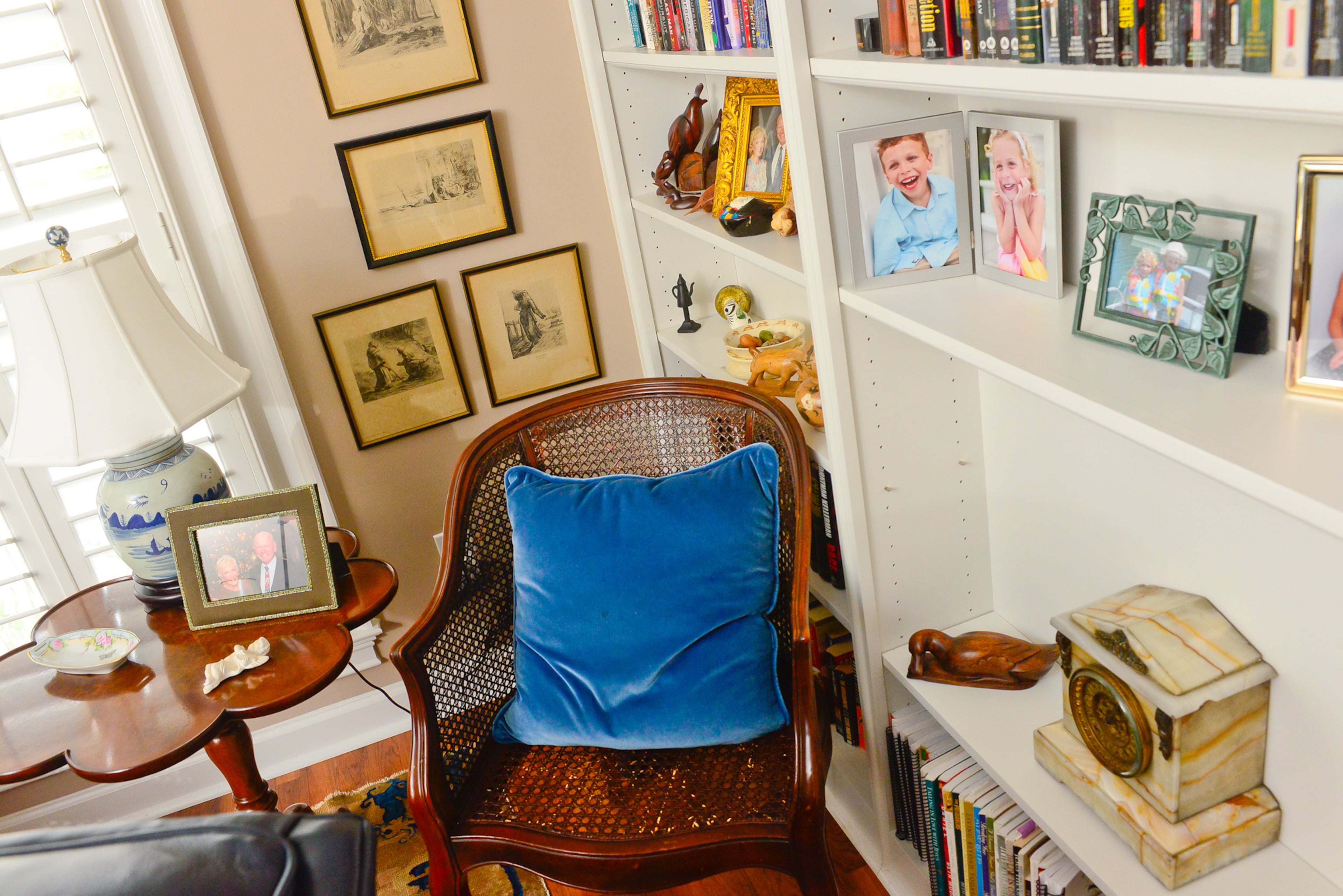Linda paired an antique replica piecrust table that she bought with her daughter-in-law with a wicker chair antique shop find to create a cozy nook in her den. Above the chair hangs a collection of wood cuts, souvenirs that Chris' father brought back from China.