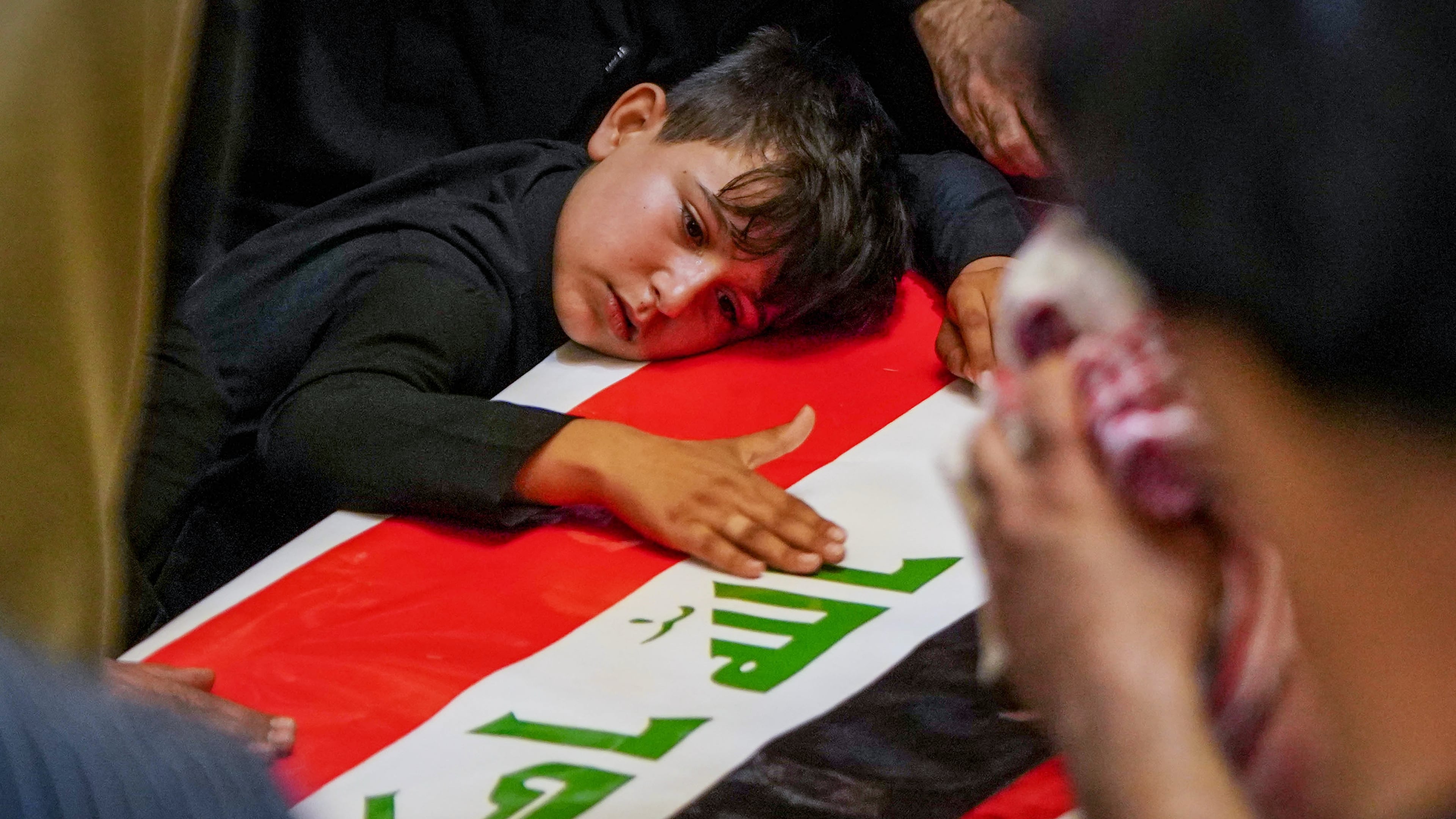 A child rests his head on the coffin of a Popular Mobilization Forces fighter draped in the Iraqi flag during a funeral for Popular Mobilization Forces fighters killed in airstrikes on PMF bases in Najaf, Iraq, Thursday, July 30, 2026. (AP Photo/Anmar Khalil)