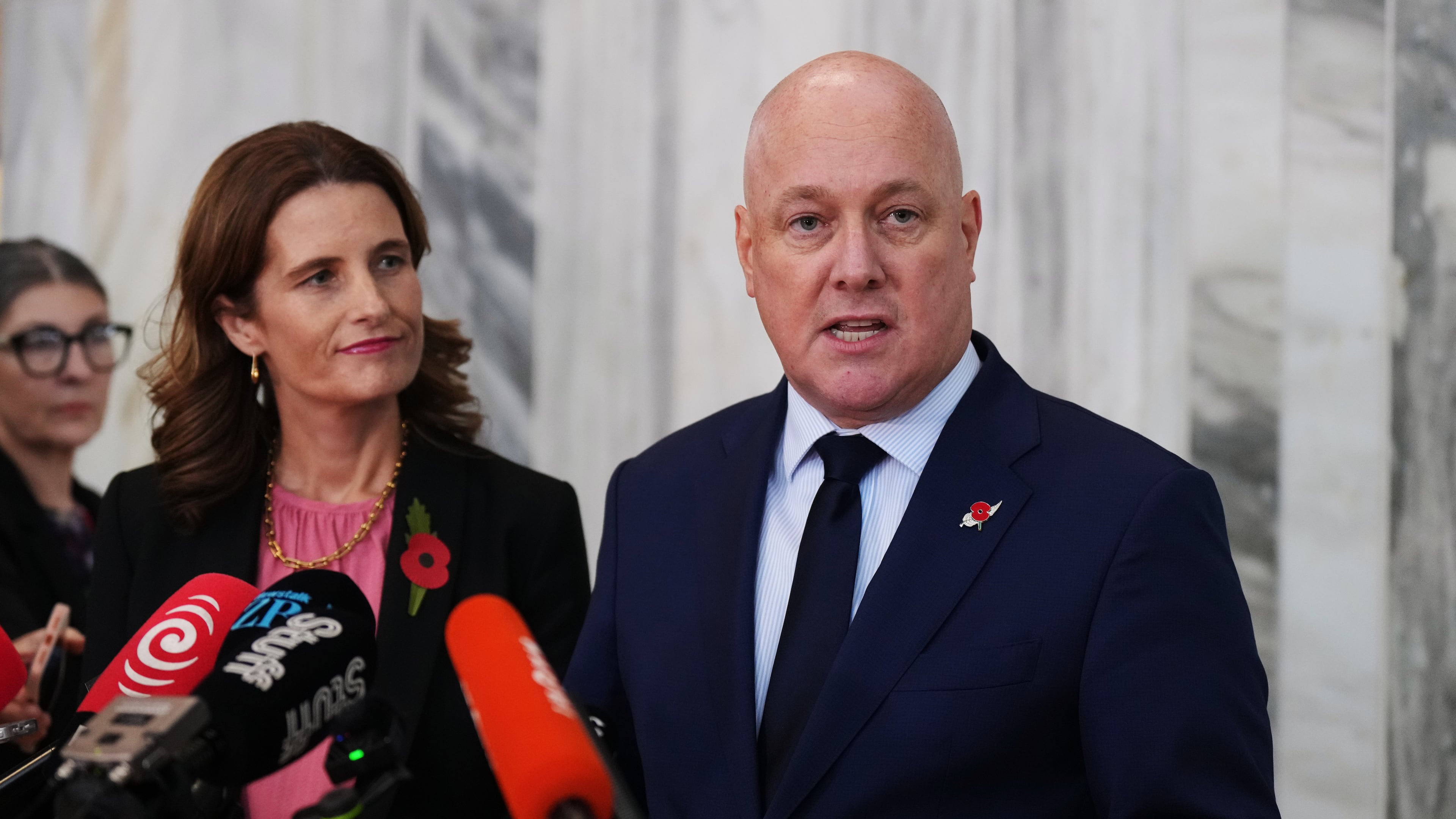 New Zealand Prime Minister Christopher Luxon, right, speaks to reporters at Parliament in Wellington, New Zealand, after a vote among his own lawmakers about his leadership of the National Party, on Tuesday. April 21 2026. (AP Photo/Charlotte Graham-McLay)