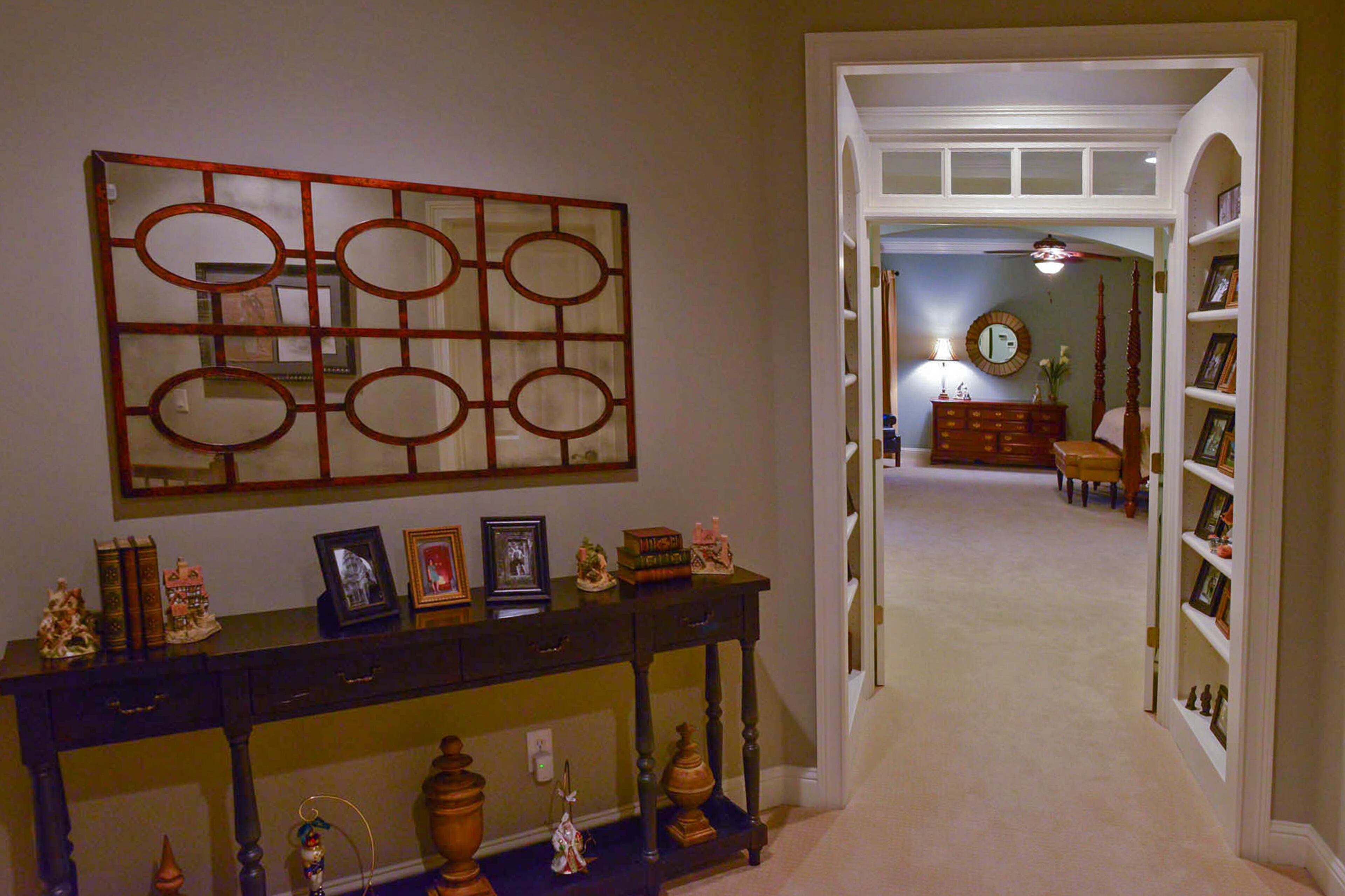 A transitional-style mirror hangs above a console decorated with pictures and decorative urns. Nutcracker and Santa ornaments span the bottom shelf. This space leads to the master suite.