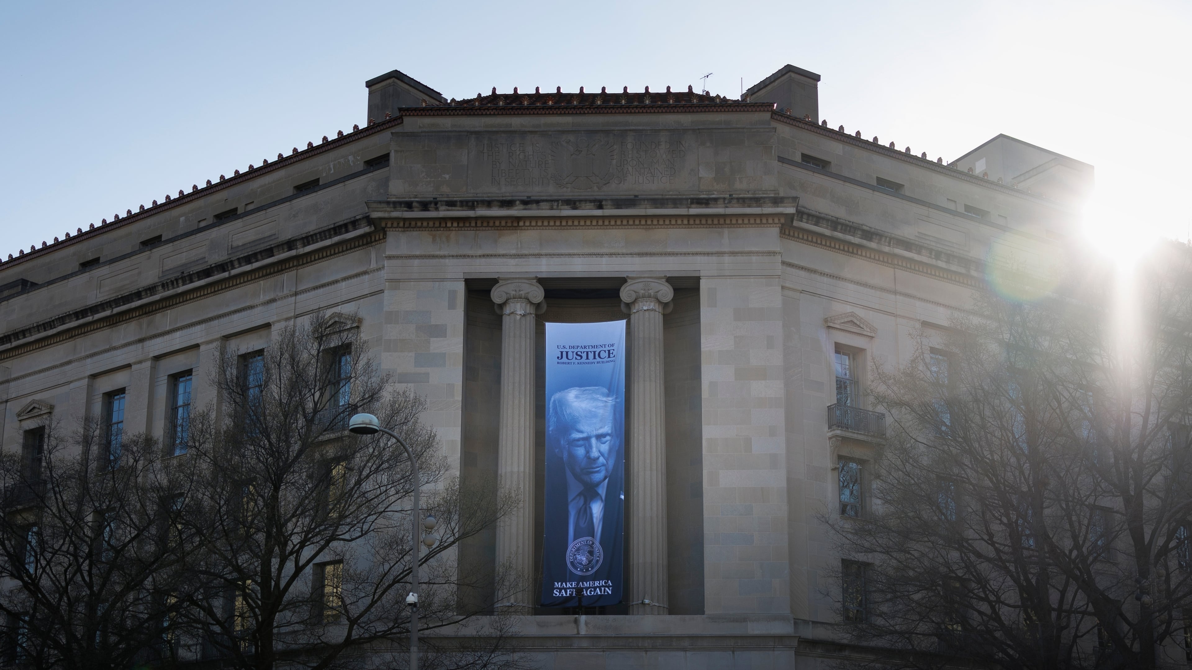A banner of President Donald Trump hangs outside the U.S. Department of Justice on Saturday, March 21, 2026, in Washington. (AP Photo/Tom Brenner)