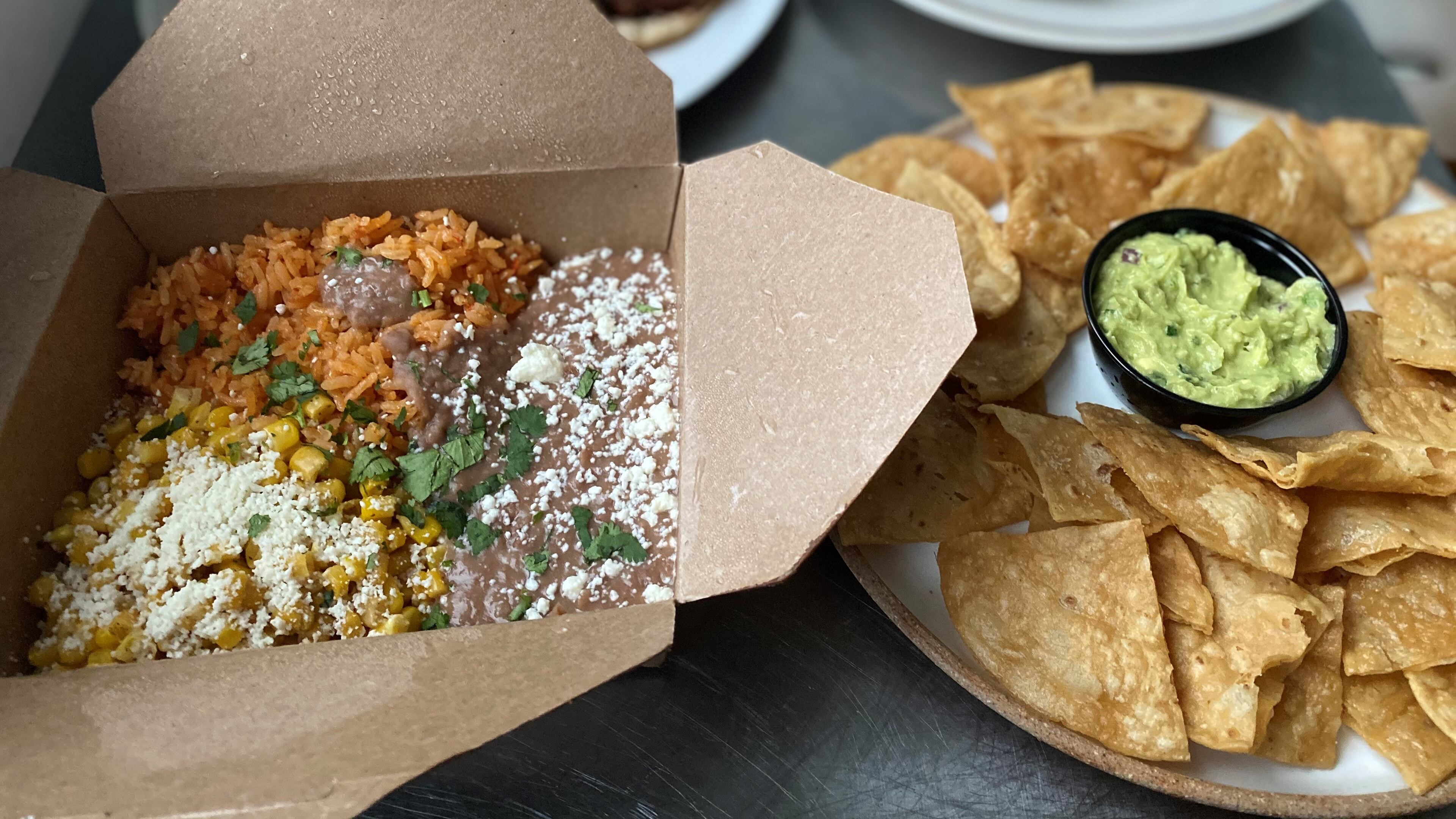 This takeout order from DaniMarco Tacos includes a box of sides (rice, beans and elote); guacamole and chips; and (in the rear) a plate of tacos and a torta with birria. Wendell Brock for The Atlanta Journal-Constitution