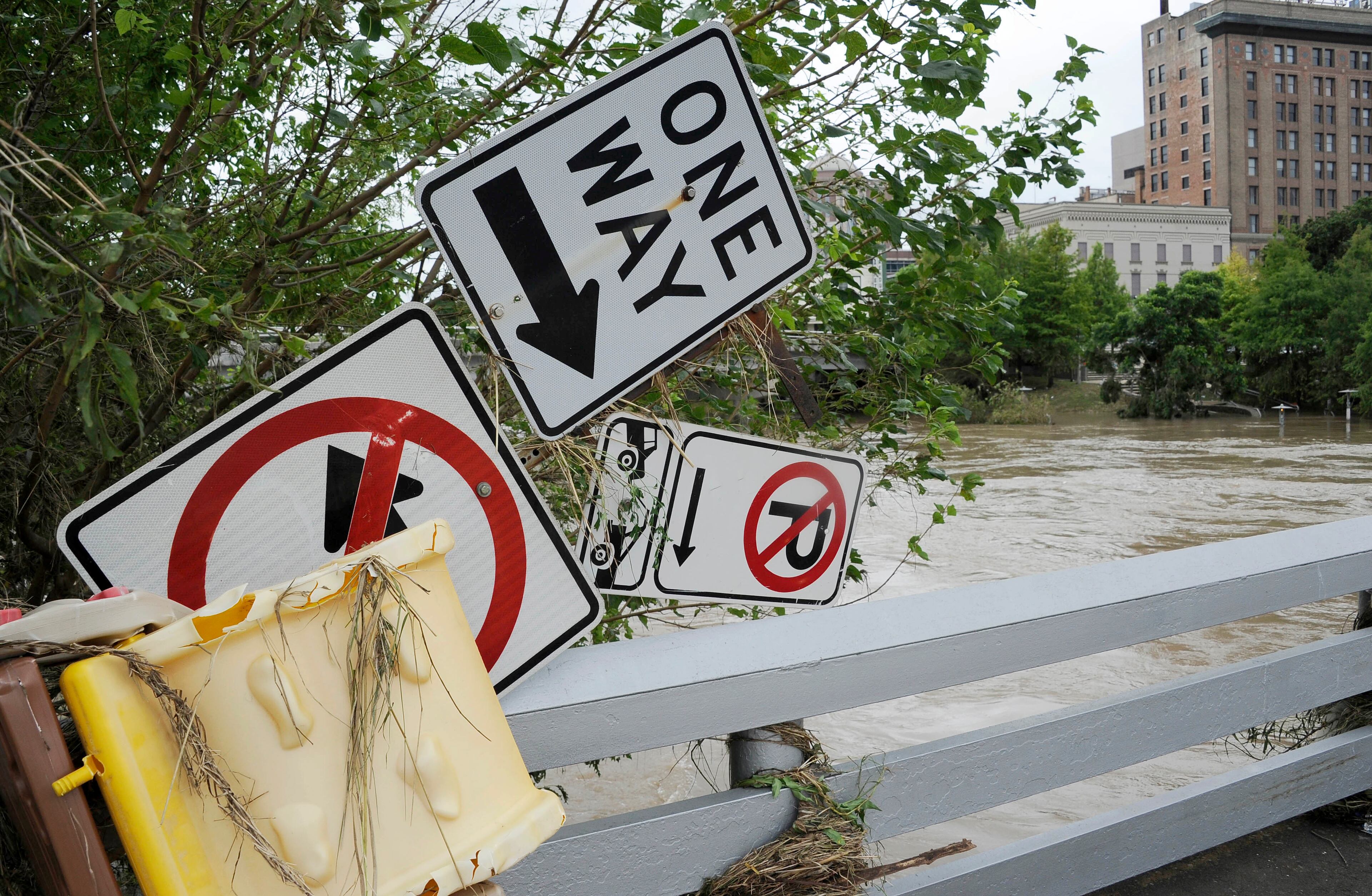A grouping of road signs perch on a bridge railing over the overrun banks of the bayou in downtown Houston, Tuesday, May 26, 2015. Floodwaters kept rising Tuesday across much of Texas as storms dumped almost another foot of rain on the Houston area, stranding hundreds of motorists and inundating the famously congested highways that serve the nation's fourth-largest city. (AP Photo/Pat Sullivan)