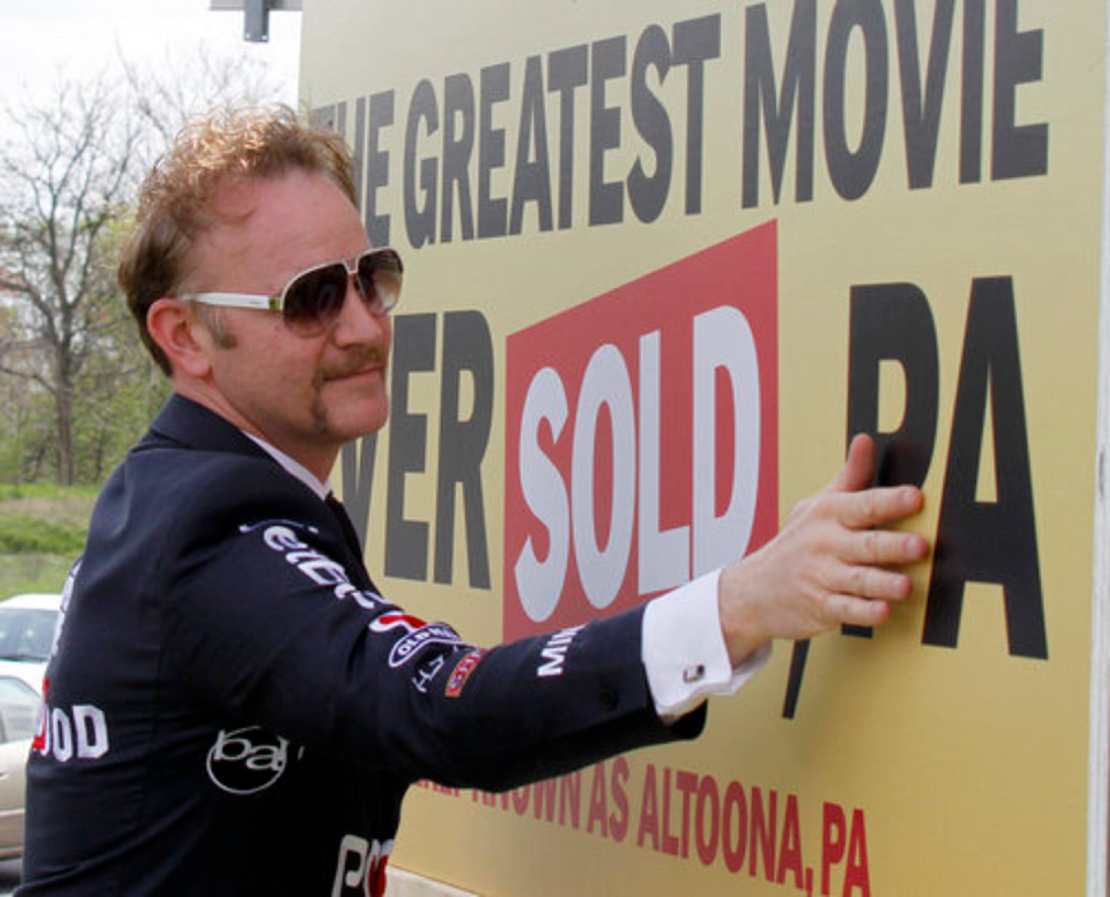 Spurlock, wearing a suit with sponsors names stitched onto it, wipes off a sign that changes the name of Altoona, Pa. to "POM Wonderful: The Greatest Movie Ever Sold."