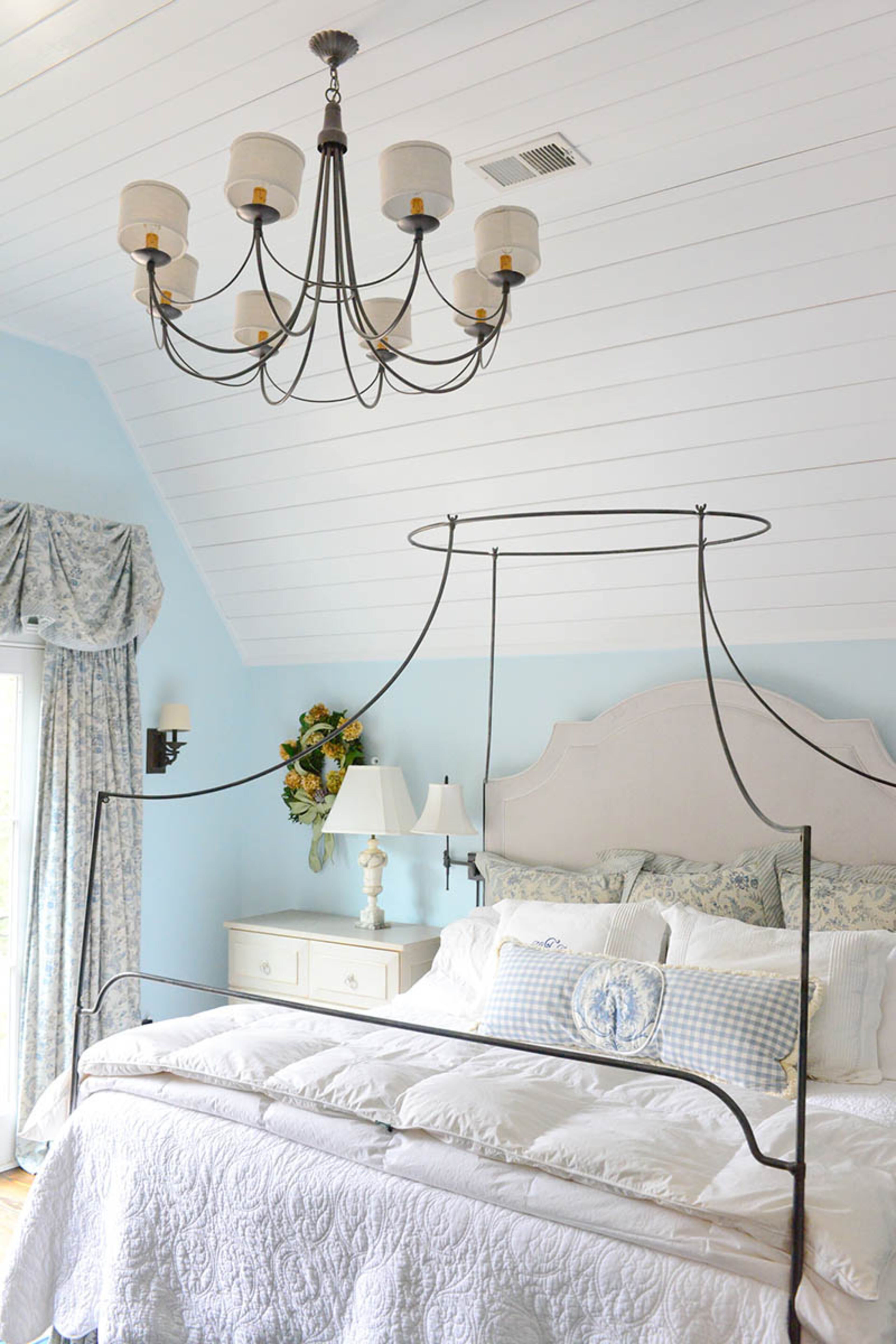 Shiplap accentuates the ceiling height and cottage feel in the master bedroom. The canopy-style bed is an Anthropologie frame found on Craigslist, and a custom headboard fits over the ironwork so the homeowners can comfortably read in bed.