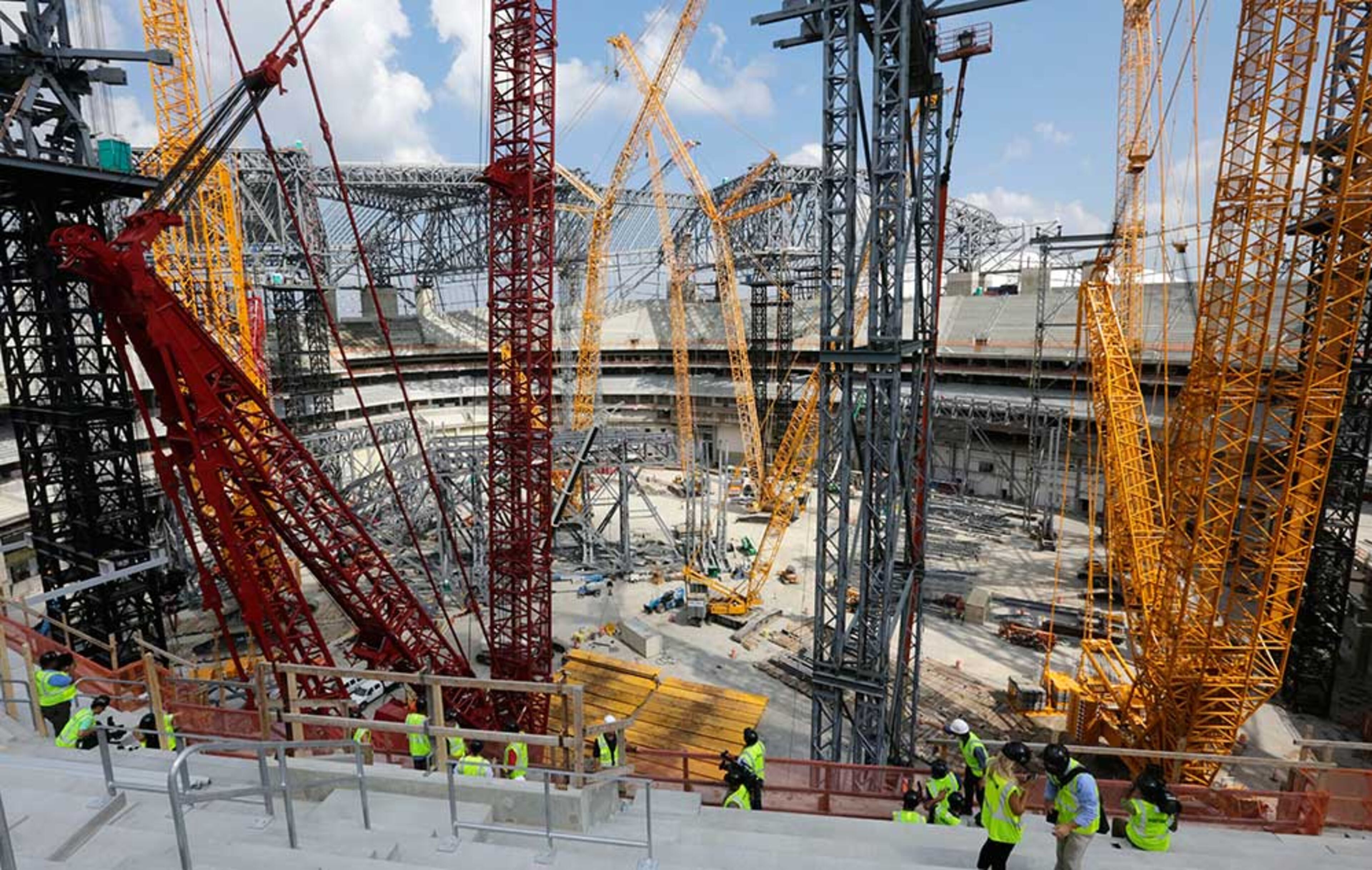 View from the upper deck shows the field level filled with steel work and cranes as tower construction and roof steel truss ground assembly continues inside the bowl.