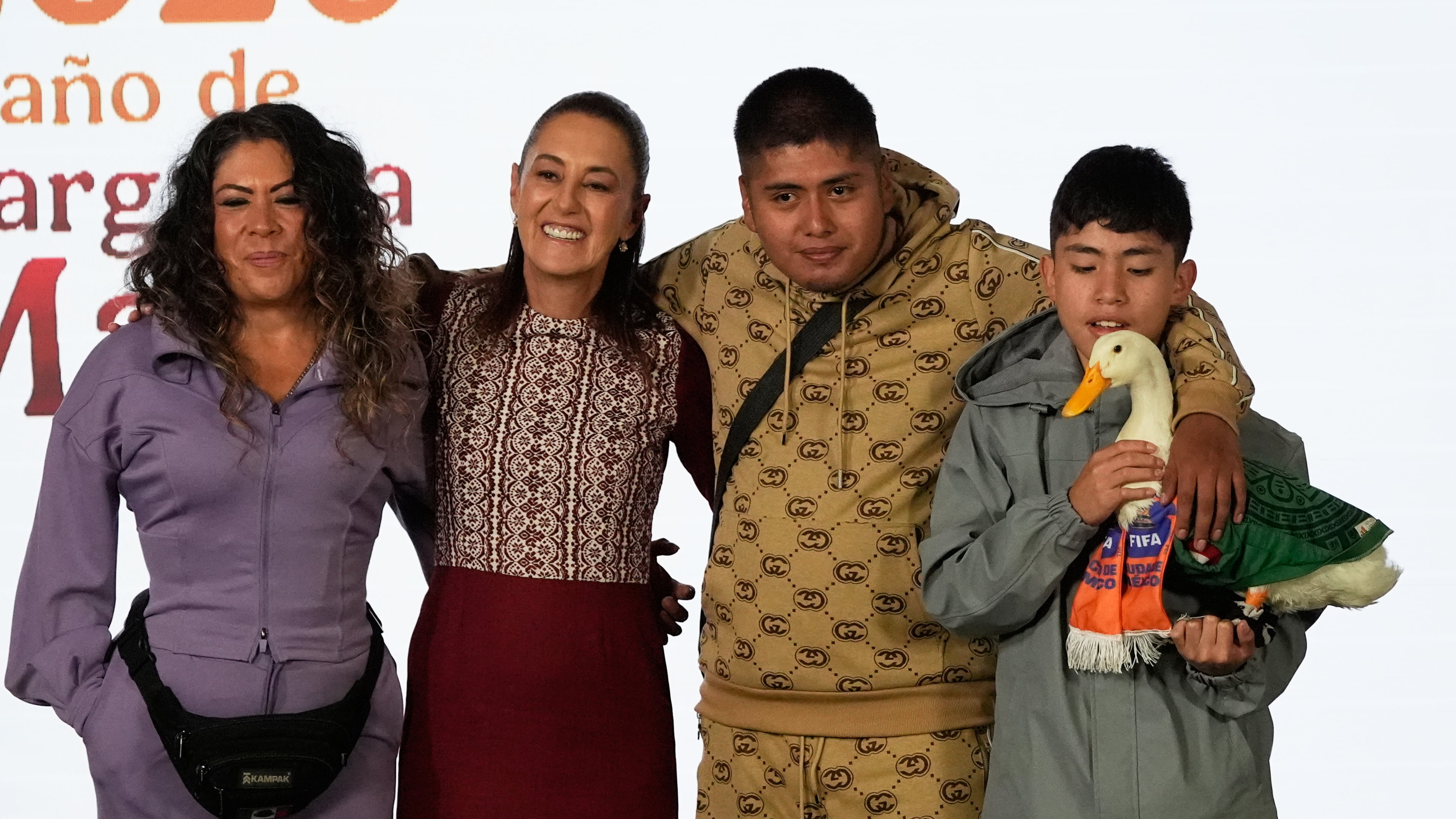 Merlin the duck, dressed in a Mexican national soccer team jersey, attends the daily press conference by Mexican President Claudia Sheinbaum, second from left, along with his caretakers Carla Gomez and her sons Carlos, and Christian who holds Merlin, at the National Palace in Mexico City, Monday, June 22, 2026. (AP Photo/Marco Ugarte)