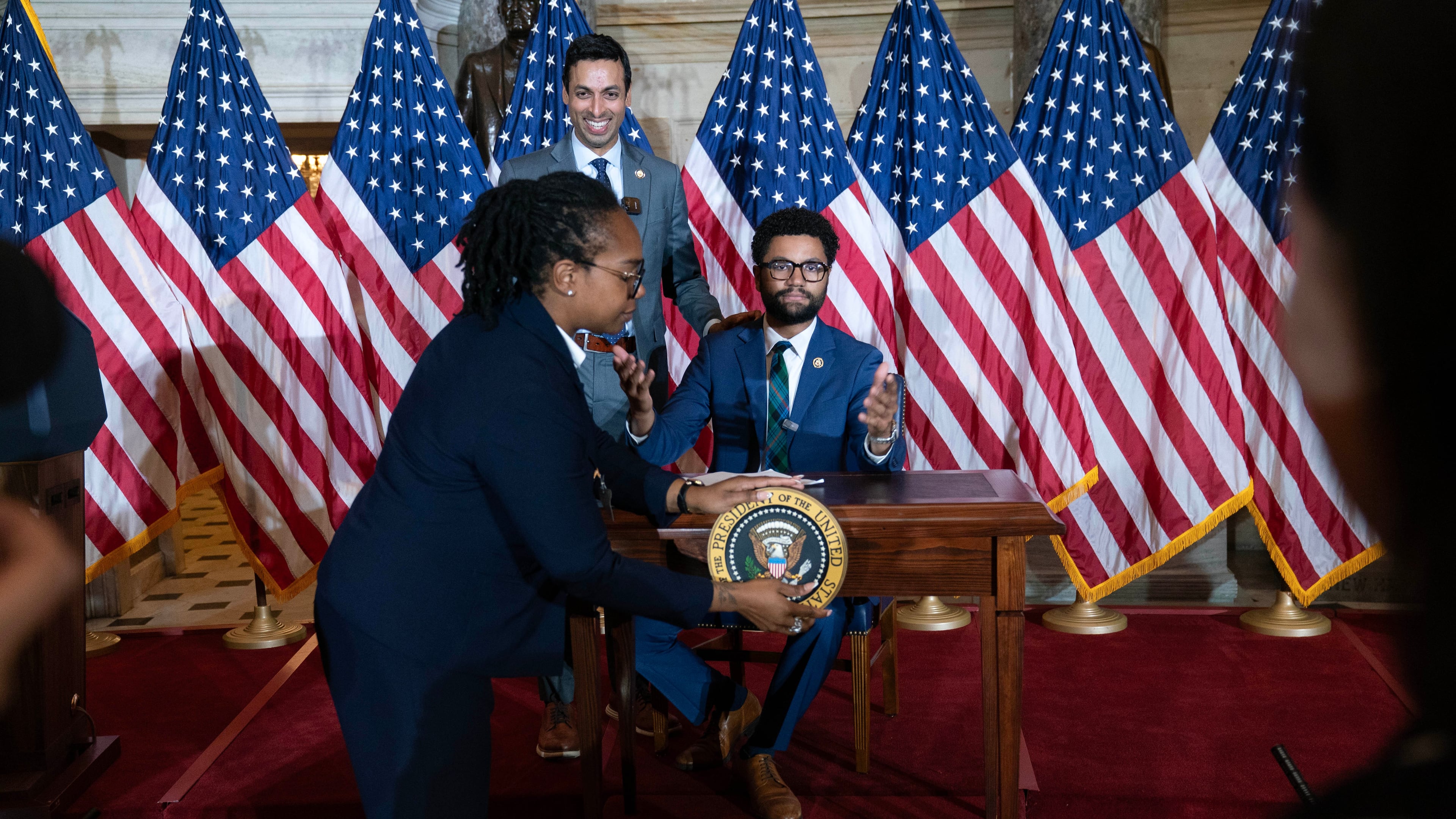 Rep. Suhas Subramanyam, D-Va., left, and Rep. Maxwell Frost D-Fla., speaks at a desk prepared for President Donald Trump as an official removes the presidential seal, after President Trump canceled the signing the bipartisan Housing Bill on the Capitol Wednesday, June 24, 2026, in Washington. (AP Photo/Jose Luis Magana)