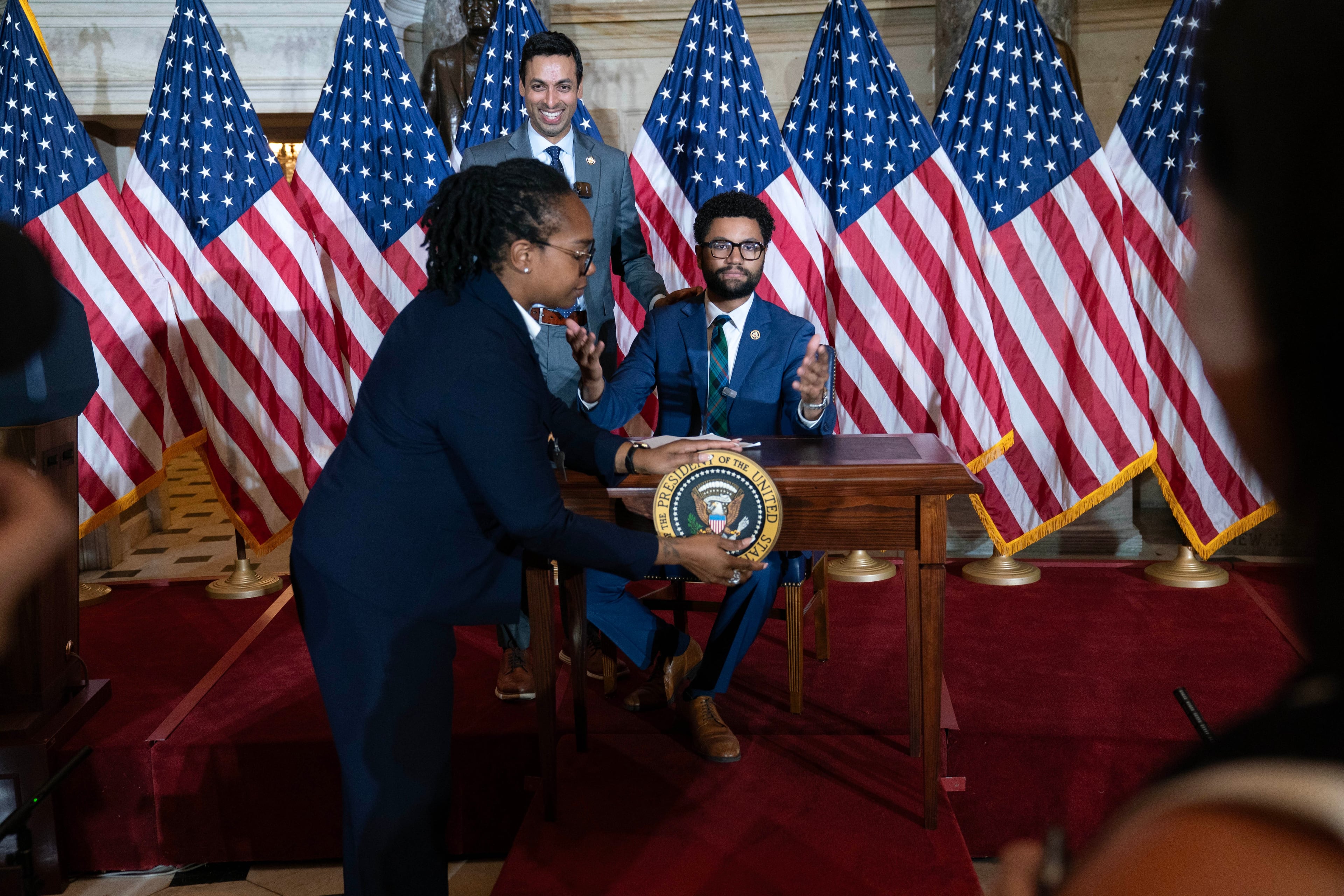 U.S. Rep. Suhas Subramanyam, D-Va. (back left), and Maxwell Frost, D-Fla., speak at a desk prepared for President Donald Trump as an official removes the presidential seal after Trump canceled the signing of a bipartisan housing bill on Wednesday. (Jose Luis Magana/AP)