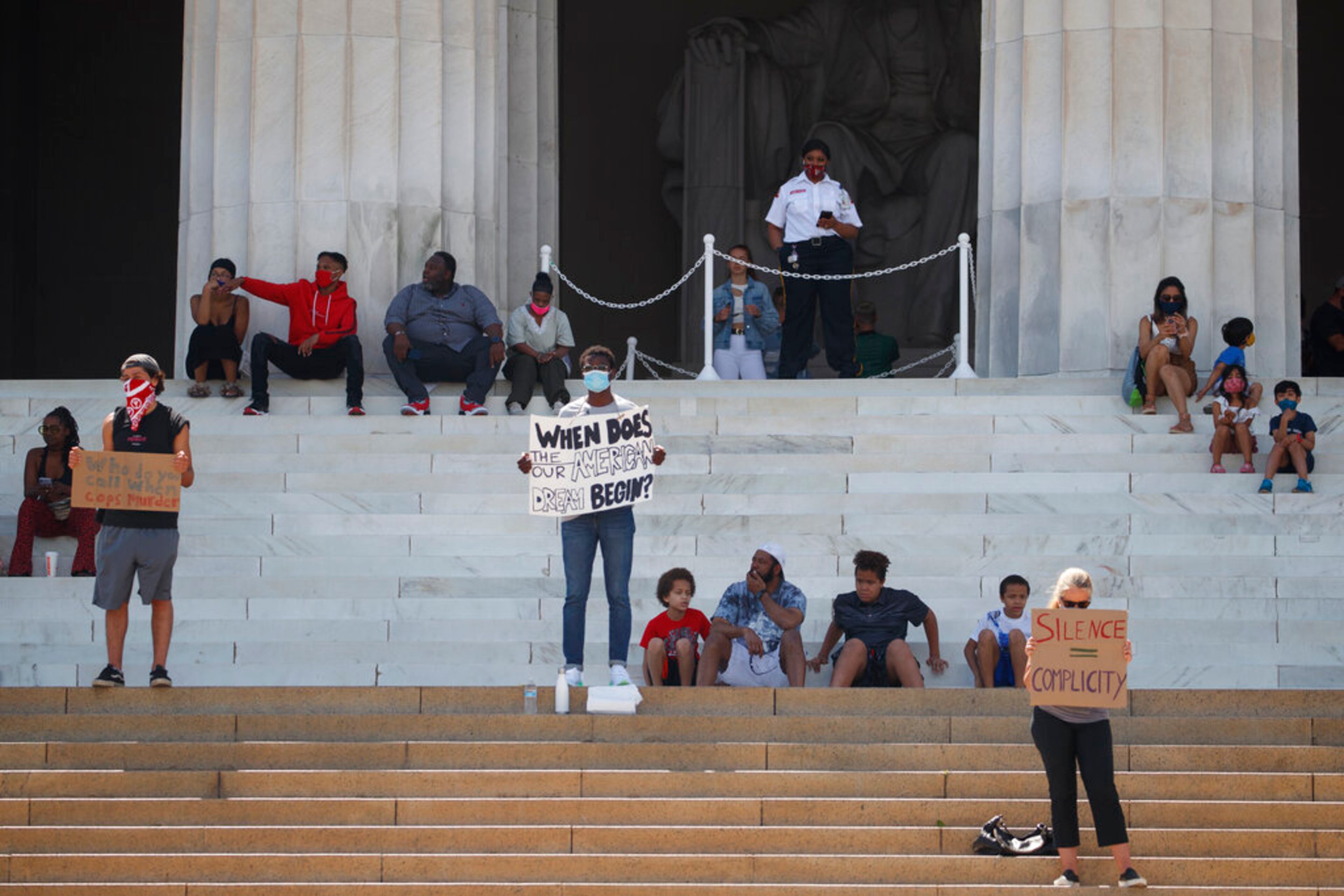 Yinka Onayemi, center, holds a sign that reads "WHEN DOES THE/OUR AMERICAN DREAM BEGIN?" and Matteo Schlitz, left, holds as sign that reads "Who do you call when cops murder" as they stand quietly on the steps of the Lincoln Memorial looking out over the National Mall in Washington, Sunday, May 31, 2020, to protests the death of George Floyd. Floyd died after being restrained by Minneapolis police officers on Memorial Day. (AP Photo/Carolyn Kaster)