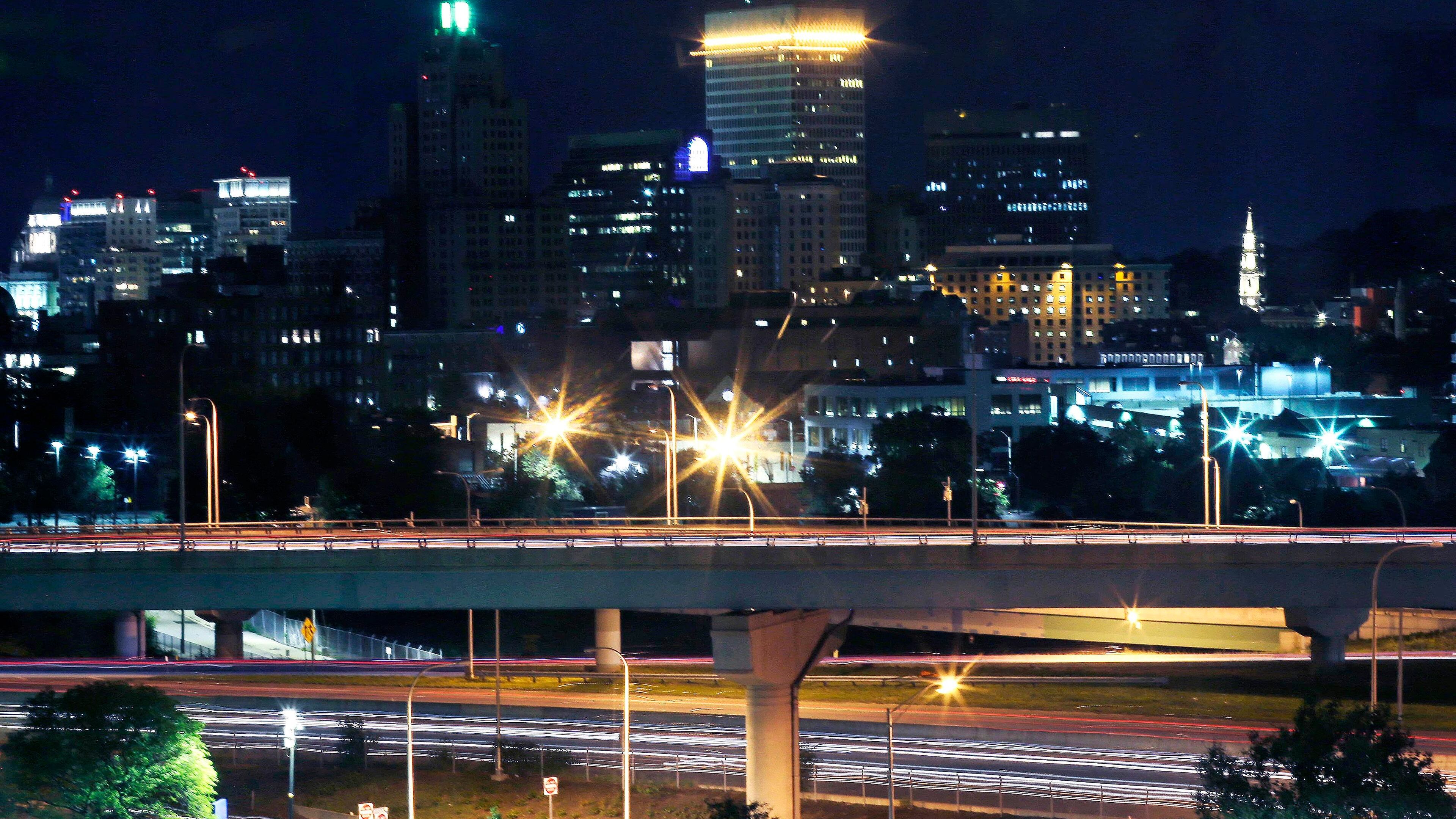 In this Wednesday, Aug. 24, 2016 photo, skyline lights illuminate downtown seen from Hasbro Children's Hospital, in Providence, R.I. For one sparkling minute each night, blinking lights from skyscrapers, tugboats, hotels, a yacht club and police cruisers send a goodnight message to sick kids inside the children’s hospital. Giddy kids inside the Hasbro Children’s Hospital wait for 8:30 p.m. each night, when invisible strangers flash lights from high-rise buildings and waterfront decks and parks. The kids get their own flashlights to return the message. (AP Photo/Charles Krupa)