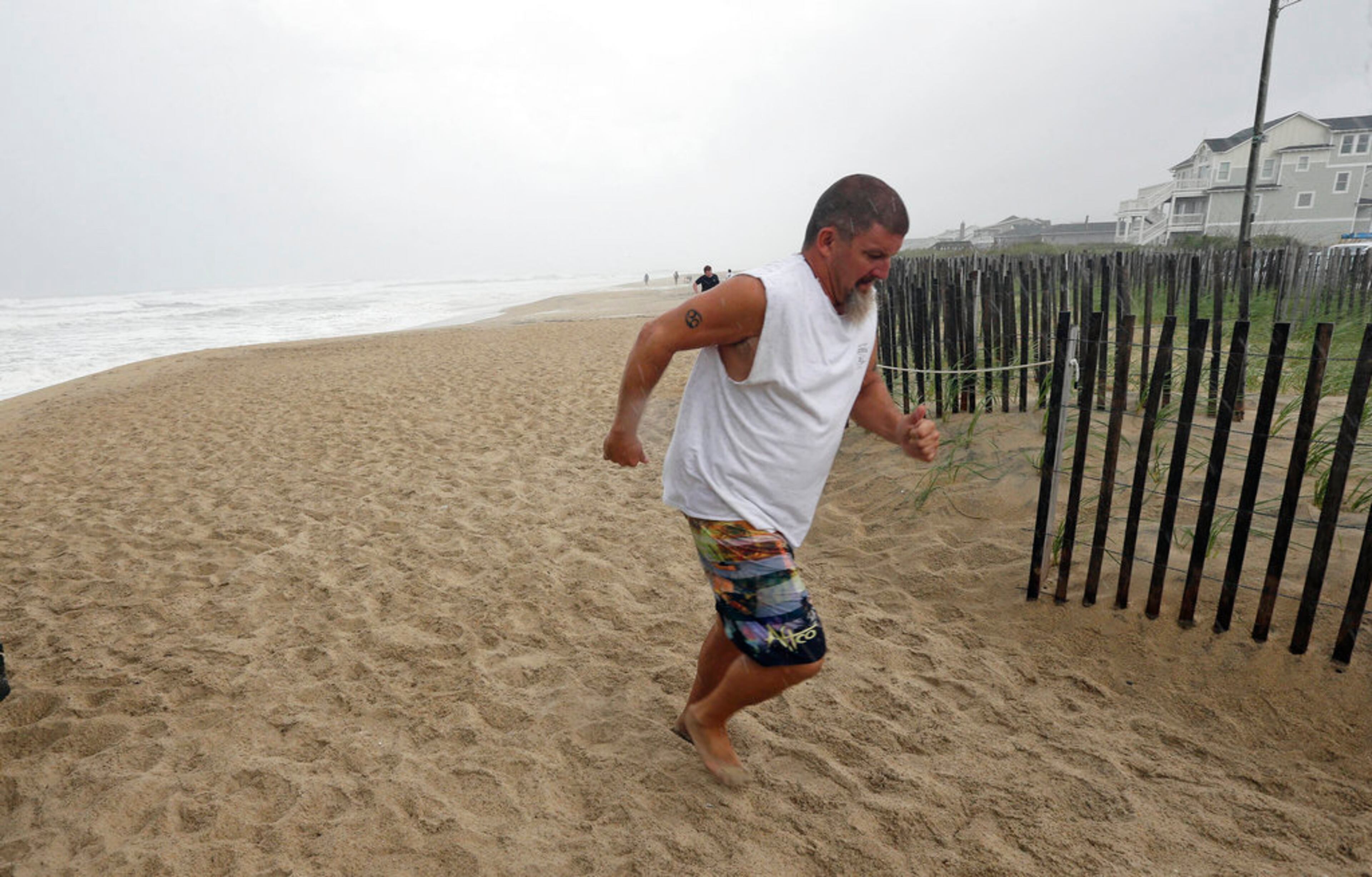 An onlooker runs from a sudden downpour in Kill Devil Hills, N.C., Thursday, Sept. 13, 2018 as Hurricane Florence approaches the east coast. (AP Photo/Gerry Broome)