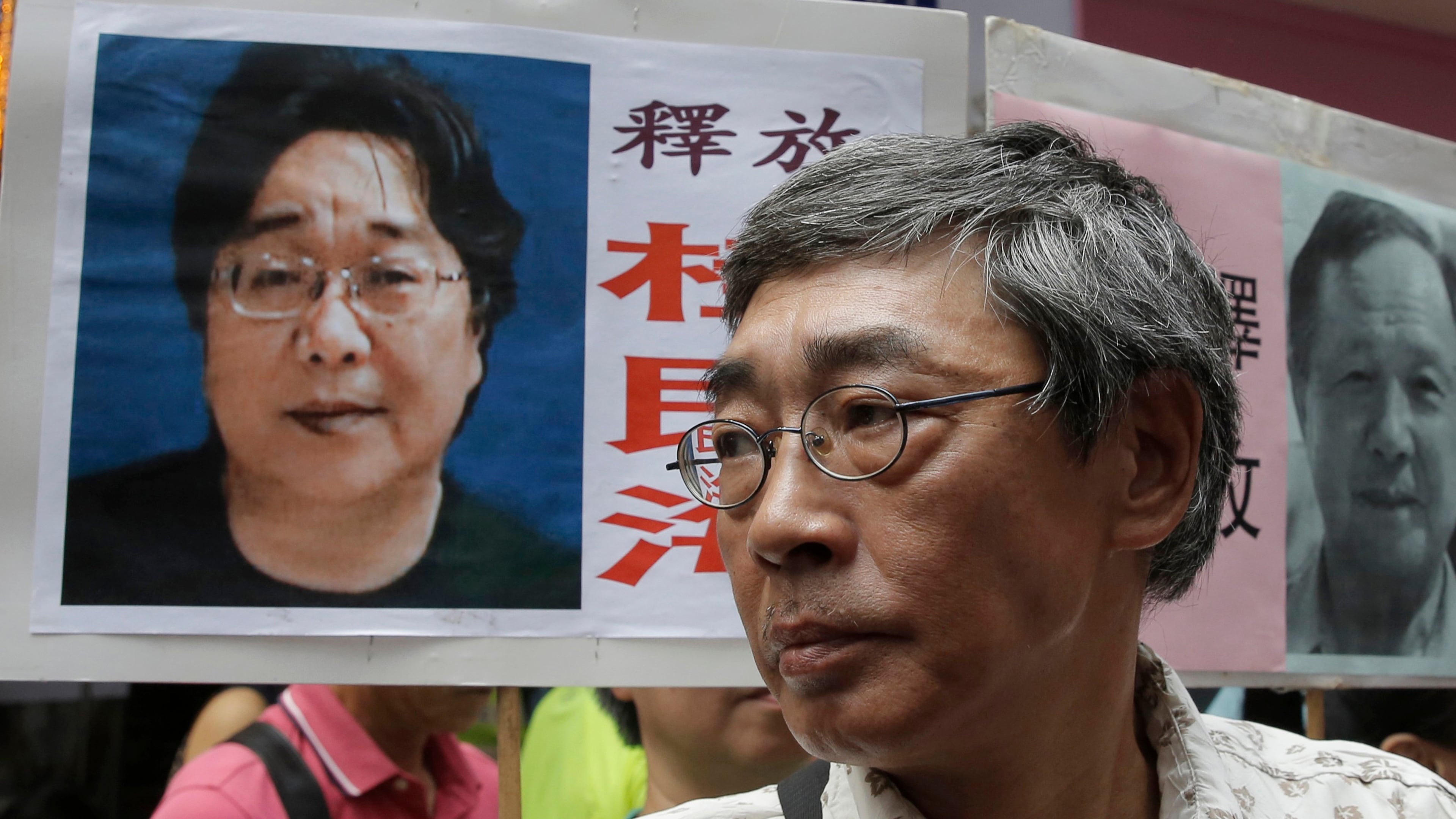 FILE - Freed Hong Kong bookseller Lam Wing-kee stands next to a placard with a picture of missing bookseller Gui Minhai, left, in front of his book store during a march in Hong Kong on June 18, 2016. (AP Photo/Kin Cheung, File)