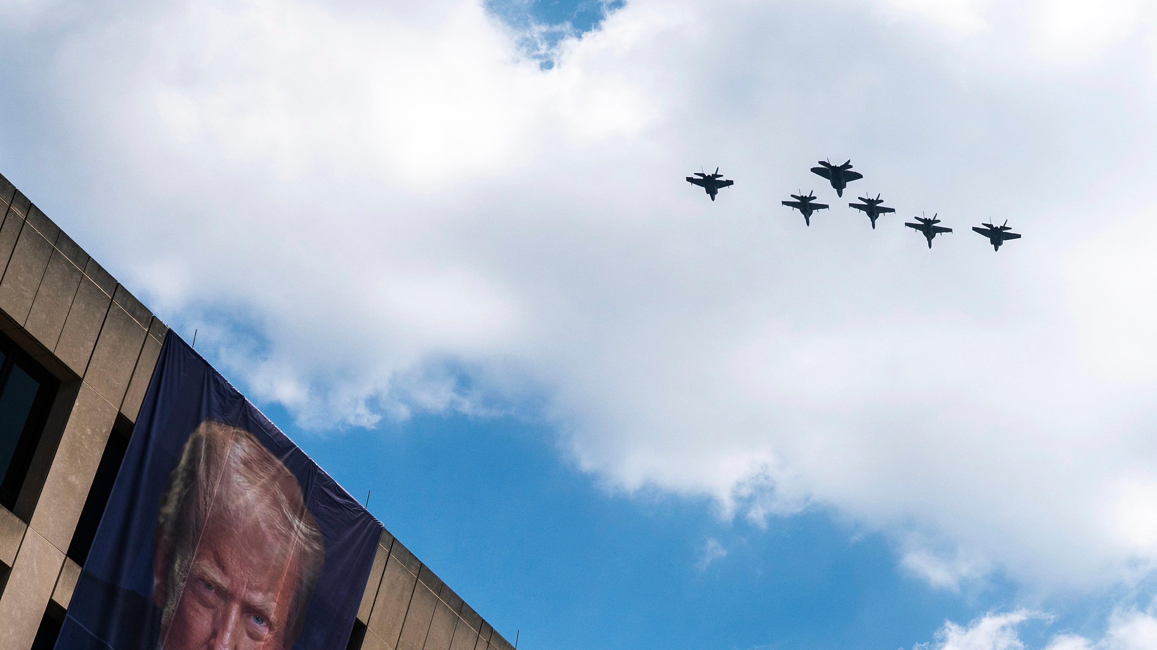 A flight of F-18s, F-35s and a F-22 fly past a picture of President Donald Trump hanging on the U.S. Department of Labor near the Great American State Fair on the National Mall, Friday, July 3, 2026, in Washington. (AP Photo/Nathan Howard)