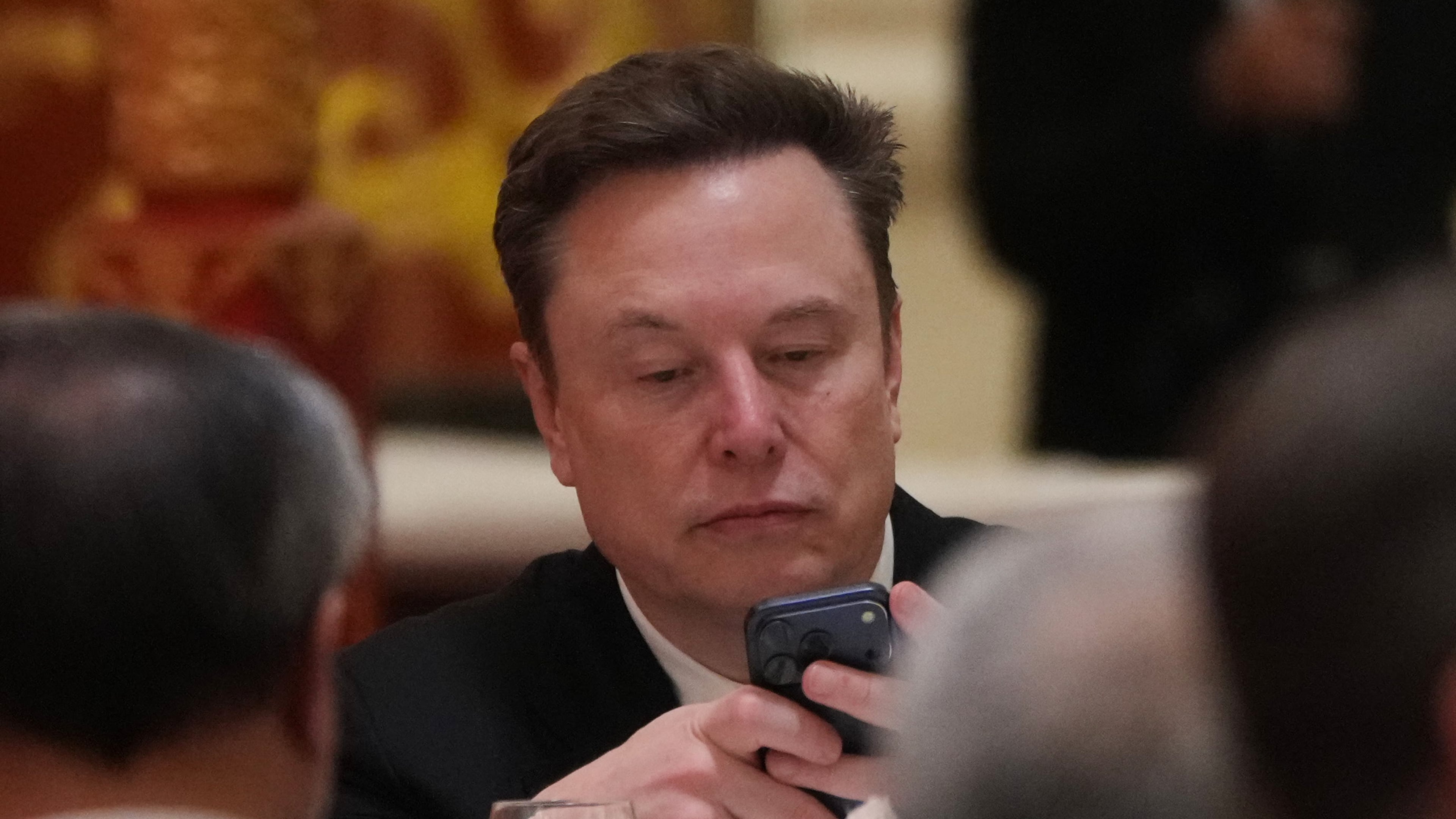 FILE - Elon Musk uses his phone during a state dinner for President Donald Trump and Chinese President Xi Jinping at the Great Hall of the People on Thursday May 14, 2026, in Beijing. (AP Photo/Mark Schiefelbein, File)