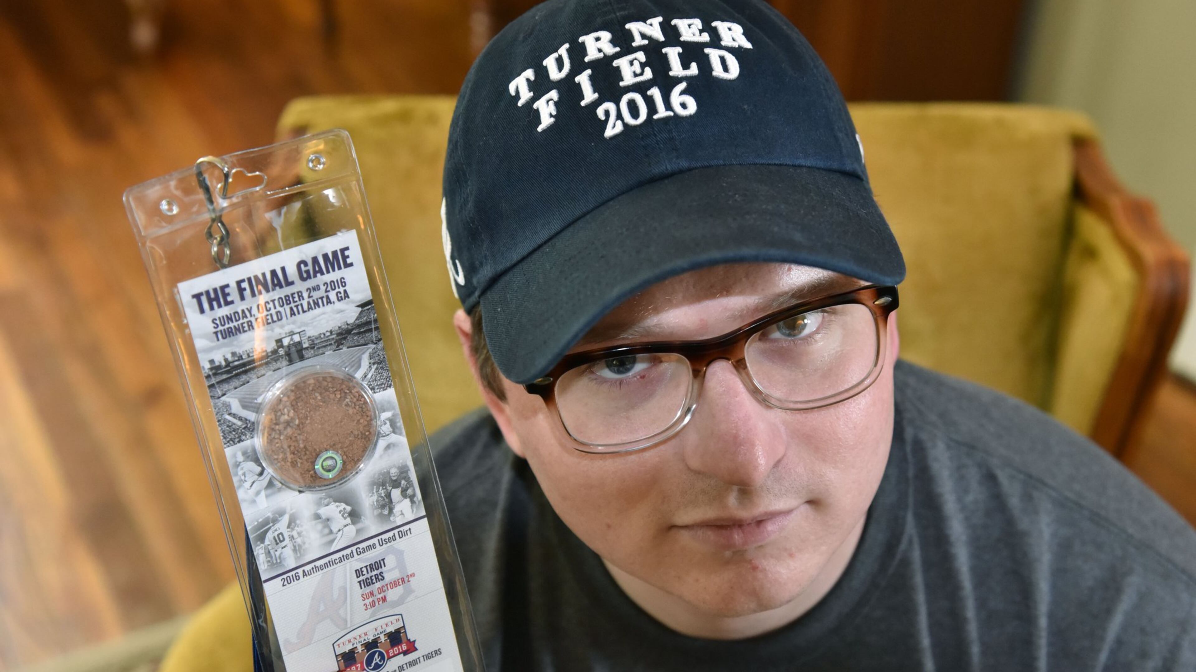 Justin Green, disgruntled Braves fan, holds the final game ticket from Turner Field at his home on Thursday. Green will be going to the game Sunday with his “Turner Field 2016” hat on in silent protest of the move. HYOSUB SHIN / HSHIN@AJC.COM