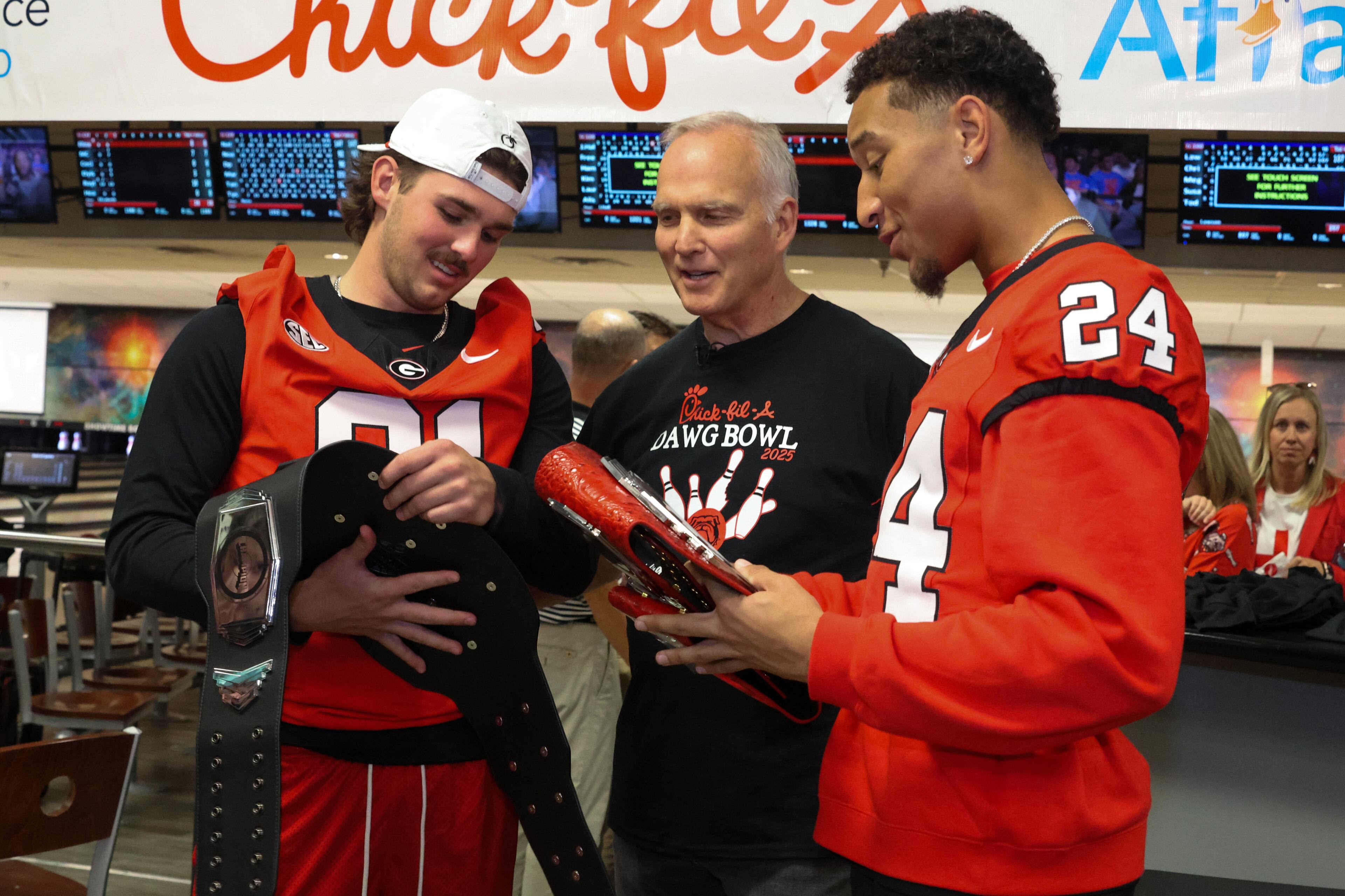 Former UGA football coach Mark Richt (center) congratulates placekicker Peyton Woodring (91) and defensive back Dominick Kelly (24) on winning belts in the third annual Chick-fil-A Dawg Bowl fundraiser for Parkinson’s and Crohn’s disease research at Showtime Bowl in Athens on Wednesday, Oct. 22, 2025. Richt, who was diagnosed with Parkinson’s disease in 2021, hosted the event. (C.J. Bartunek for the AJC)