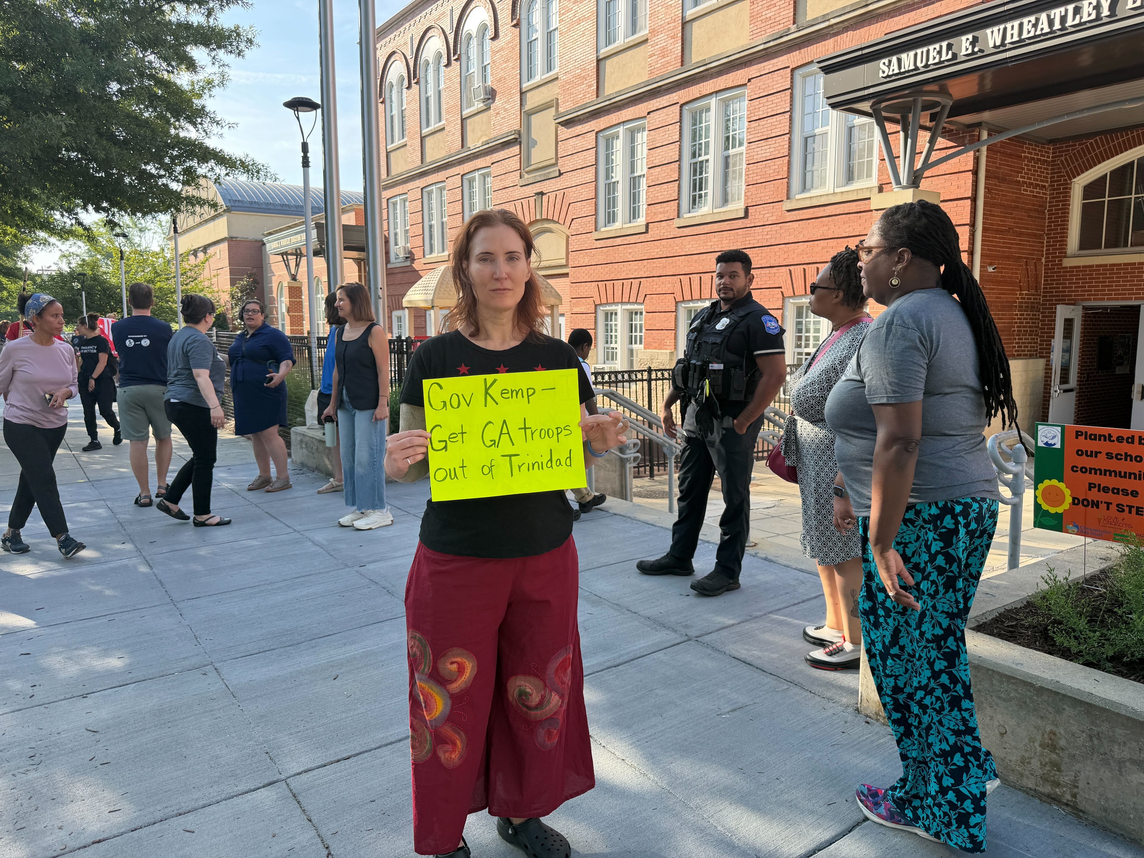 Karen Wheeler, a Washington resident who is active with the Free DC movement, participated in a rally outside of the Wheatley Education Campus on Aug. 26, 2026, where she held a sign asking Gov. Brian Kemp to remove Georgia National Guard troops seen patrolling in the Trinidad neighborhood. (Tia Mitchell/AJC)
