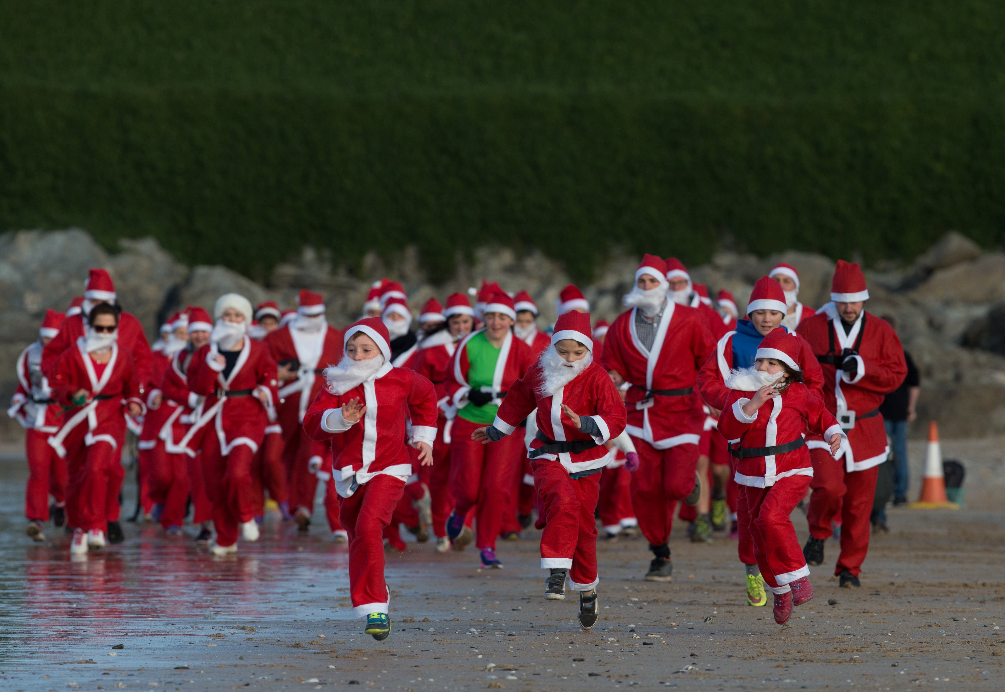 NEWQUAY, ENGLAND - DECEMBER 04: People dressed as Santa take part in the beach fun run as part of the Santa Run and Surf 2016 at Fistral Beach in Newquay on December 4, 2016 in Cornwall, England. Now in its third year, the santa surf and fun run is organised by Fistral Surf Center and Cornwall Hospice Care and raises funds for local charities. (Photo by Matt Cardy/Getty Images)