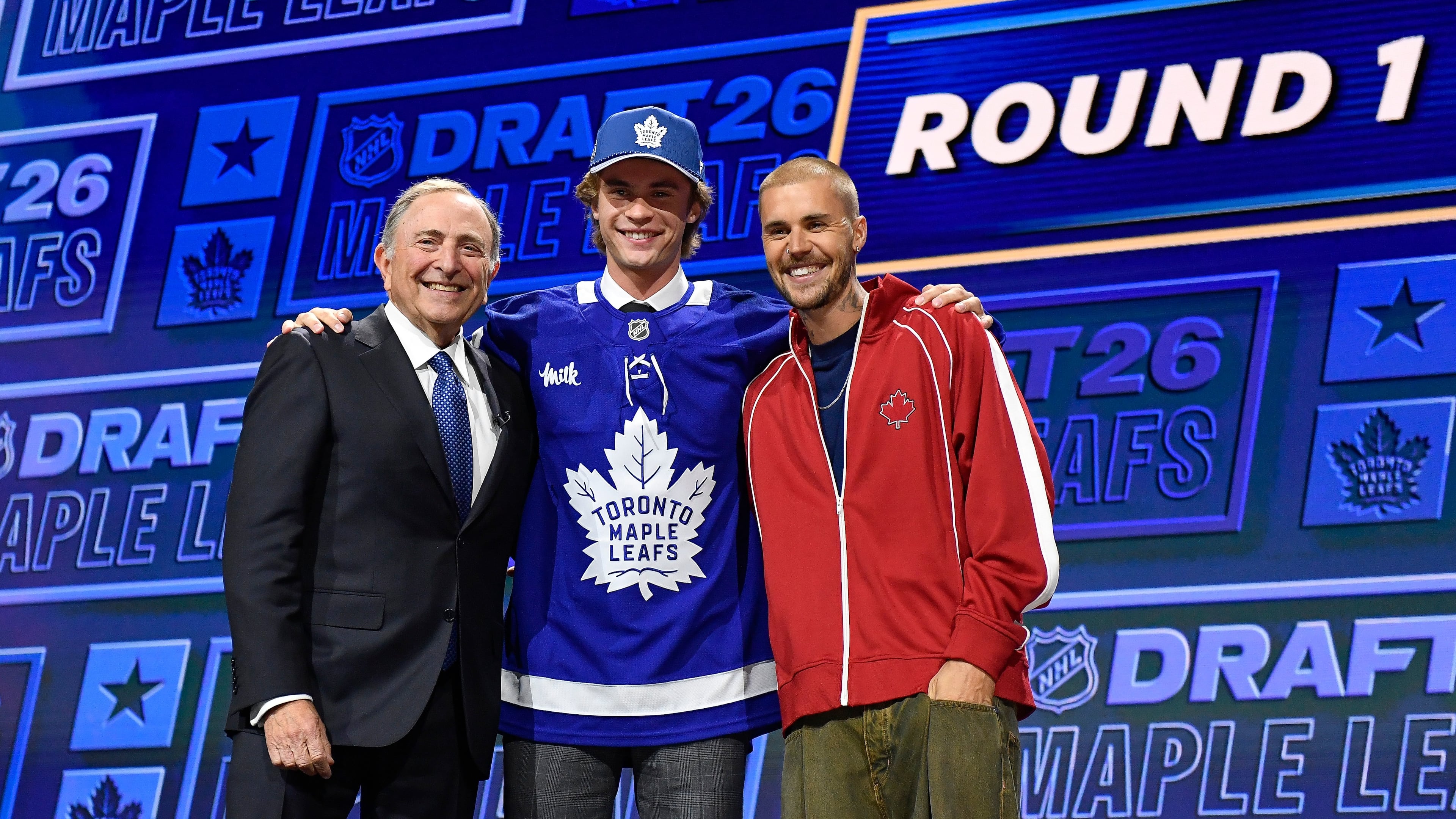 Gavin McKenna, center, stands with NHL Commissioner Gary Bettman, left, and singer Justin Bieber, right, after being drafted by the Toronto Maple Leafs during the NHL hockey draft Friday, June 26, 2026, in Buffalo, N.Y. (AP Photo/Adrian Kraus)