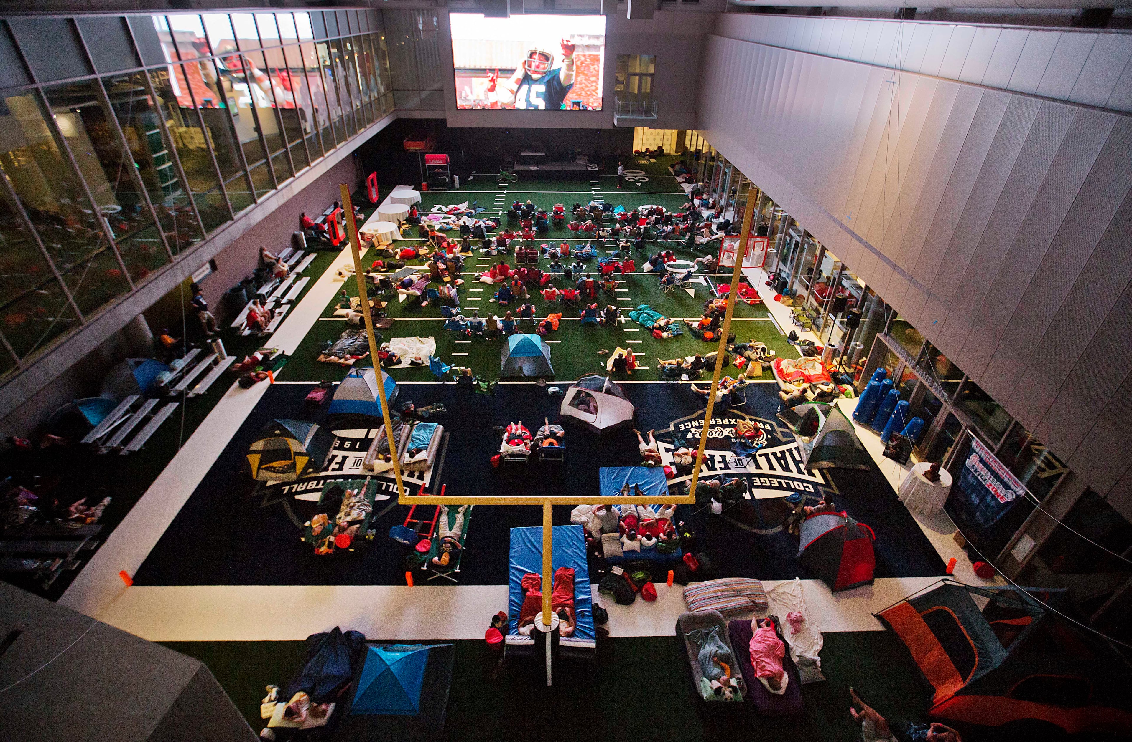 Guests watch from the turf as the movie "Rudy" is plays during a sleepover in the College Football Hall of Fame in the early hours, Thursday, Aug. 14, 2014, in Atlanta. The crowd of 200 who came from as far away as Hawaii were among the first to experience the College Football Hall of Fame and Chick-fil-A Fan experience before it opened to the public on Aug. 23. (AP Photo/David Goldman)