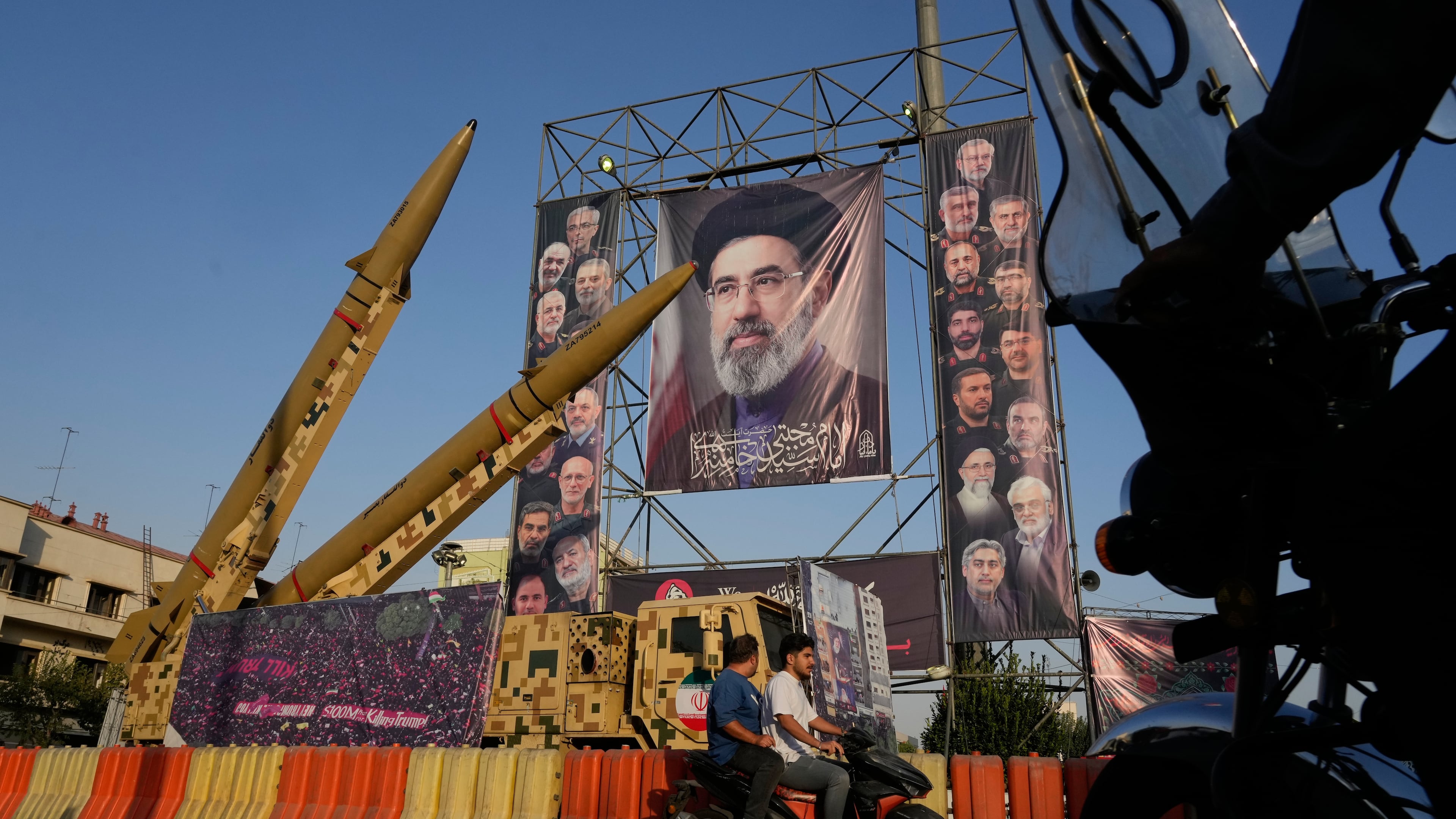Motorbikes drive past Iranian missiles and banners showing portraits of the Iranian Supreme Leader Ayatollah Mojtaba Khamenei, center, and the late armed forces commanders and nuclear scientists, who were killed in Israeli and U.S. strikes, displayed in a military exhibition commemorating the anniversary of the start of the 1980-88 Iraq-Iran war at Baharestan Square, in Tehran, Monday, Sept. 28, 2026. (AP Photo/Vahid Salemi)