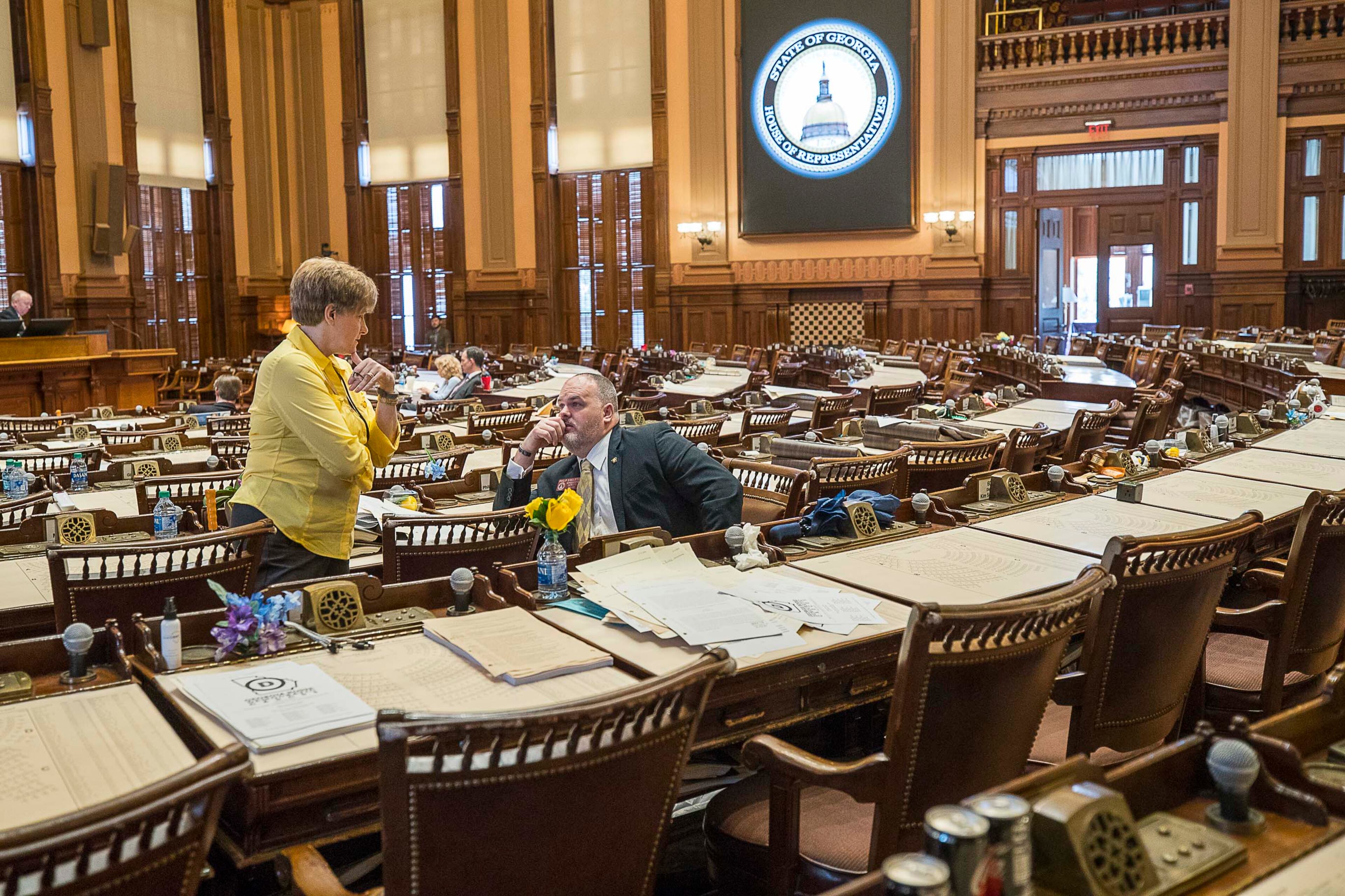 Georgia Rep. Sheri Gilligan, left, R-Cumming, and Rep. Philip Singleton, right, R-Sharpsburg, talk among a sea of empty desks on March 13, 2020, the last day that the Georgia Legislature met before the session was suspended. (ALYSSA POINTER/ALYSSA.POINTER@AJC.COM)