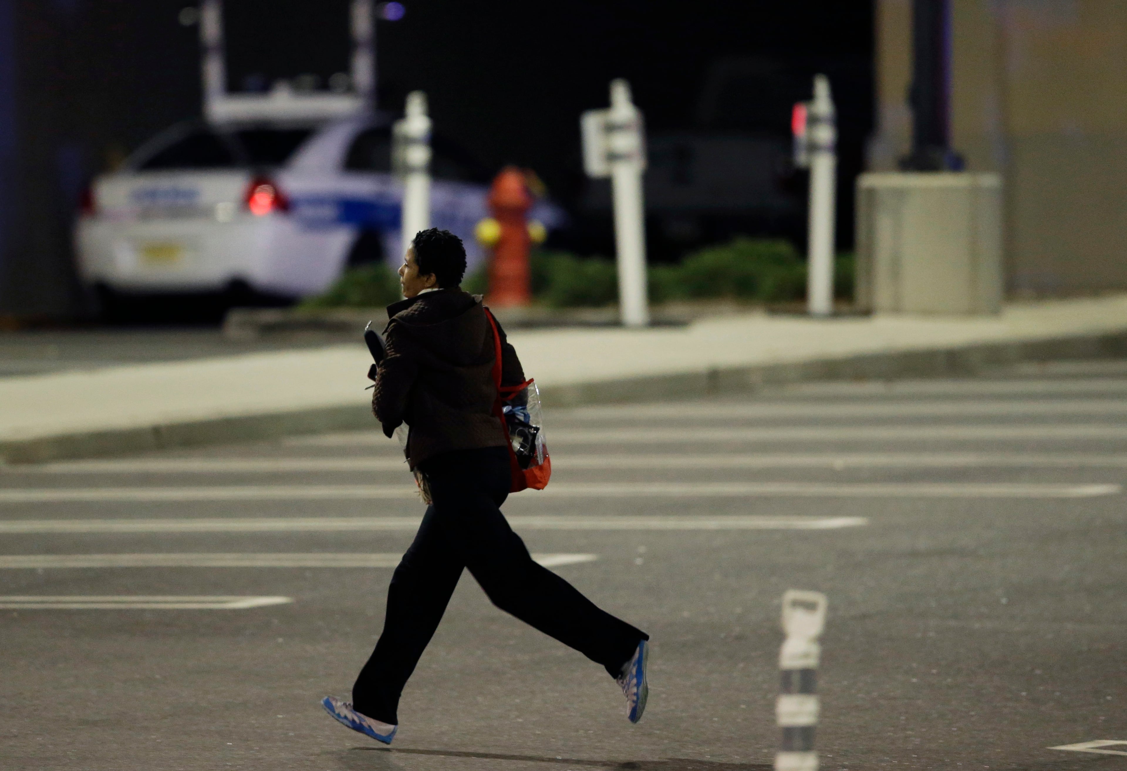 A woman runs in the parking lot of the Garden State Plaza Mall following reports of a shooter, Monday, Nov. 4, 2013, in Paramus, N.J. Hundreds of law enforcement officers converged on the mall Monday night after witnesses said multiple shots were fired there. (AP Photo/Julio Cortez)